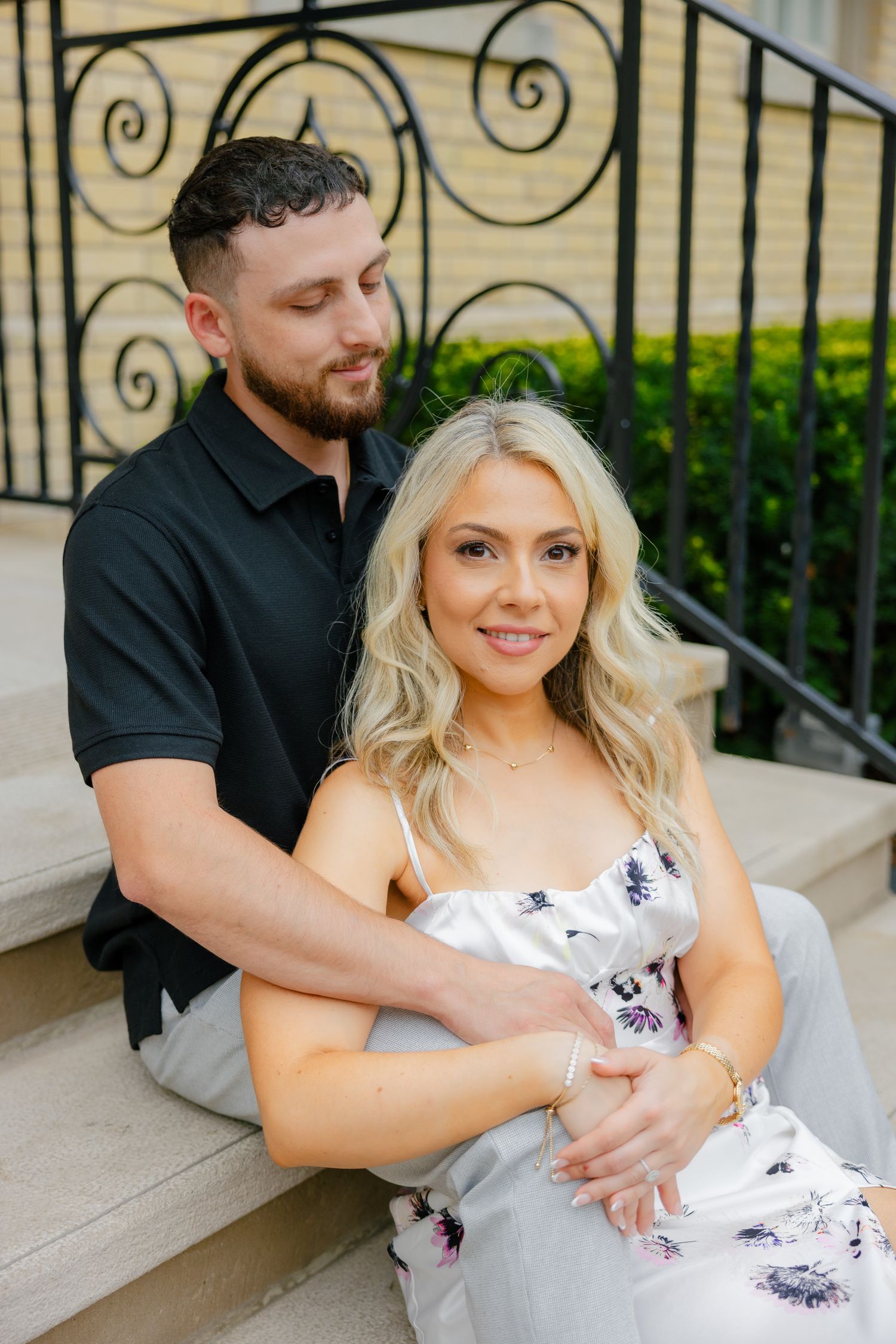 A tender moment captured of a couple sitting on stone steps against decorative railings.