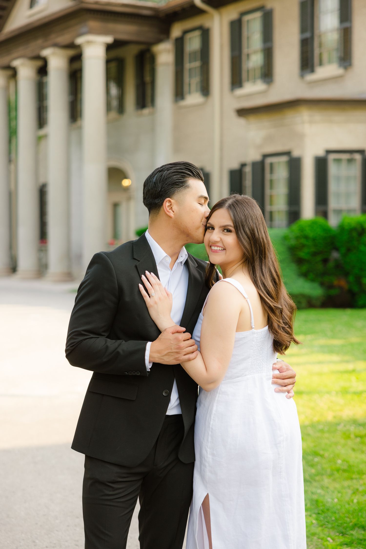Elegant couple embraces in front of historic mansion with columns during sunset photo session.