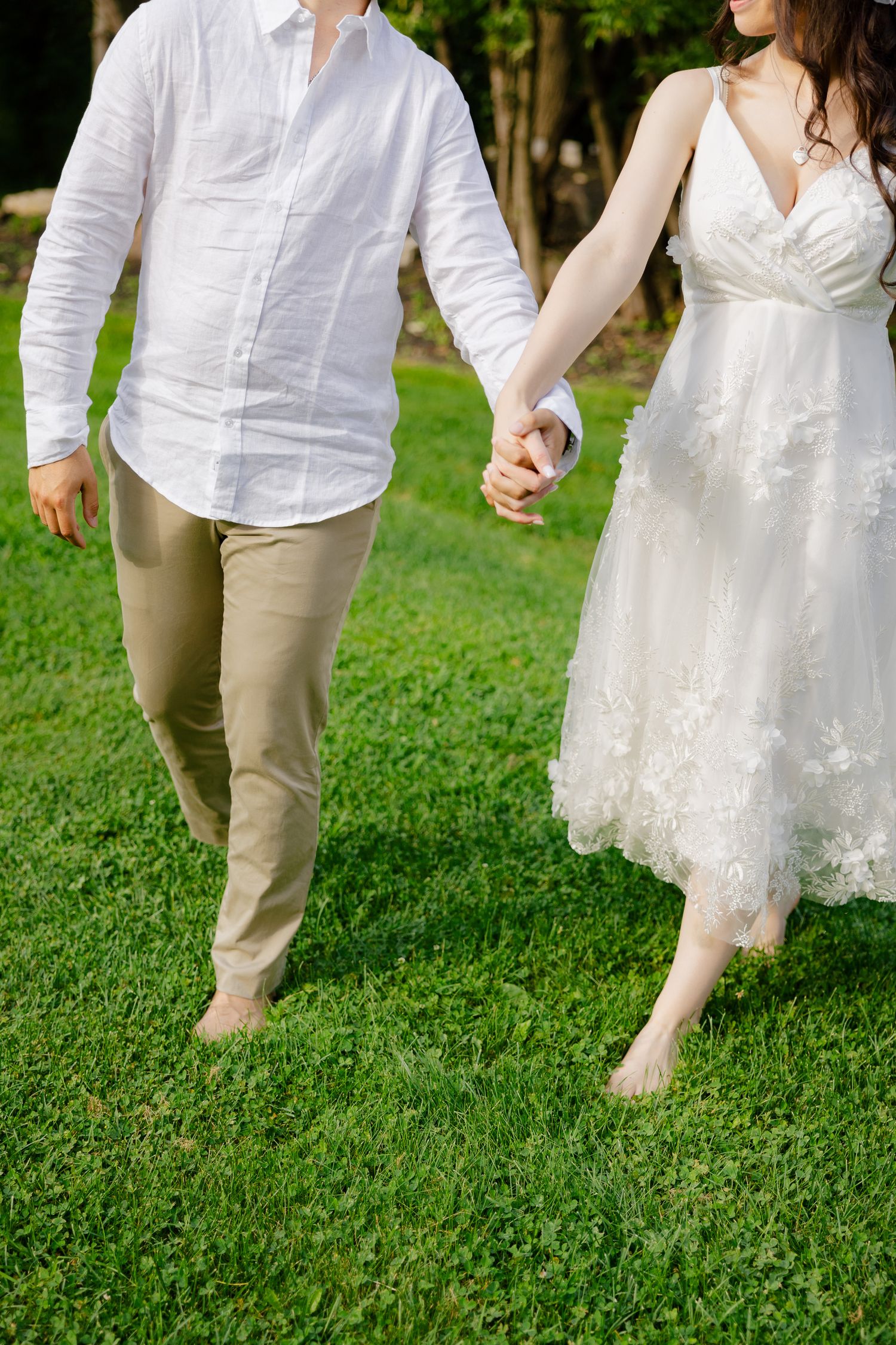 A close-up of barefoot newlyweds walking hand in hand on green grass.