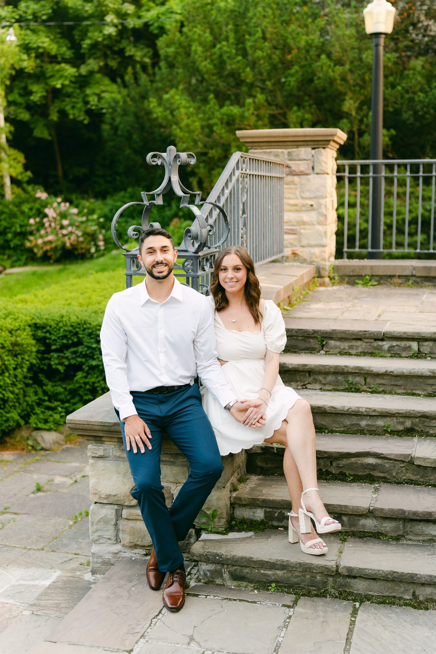 A romantic outdoor portrait session featuring a couple sitting on stone steps in a garden setting.