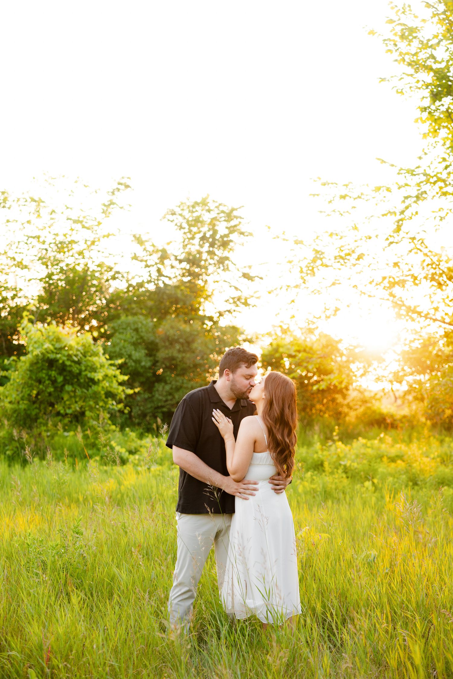Intimate portrait of couple against glowing sunset in meadow with wildflowers.