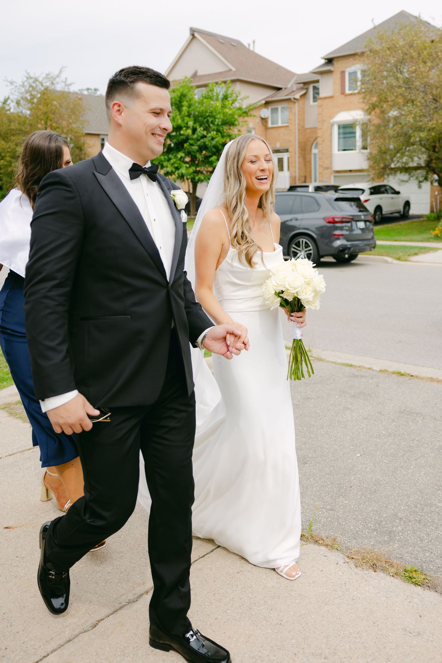 Newlyweds walking together on sidewalk in elegant wedding attire.