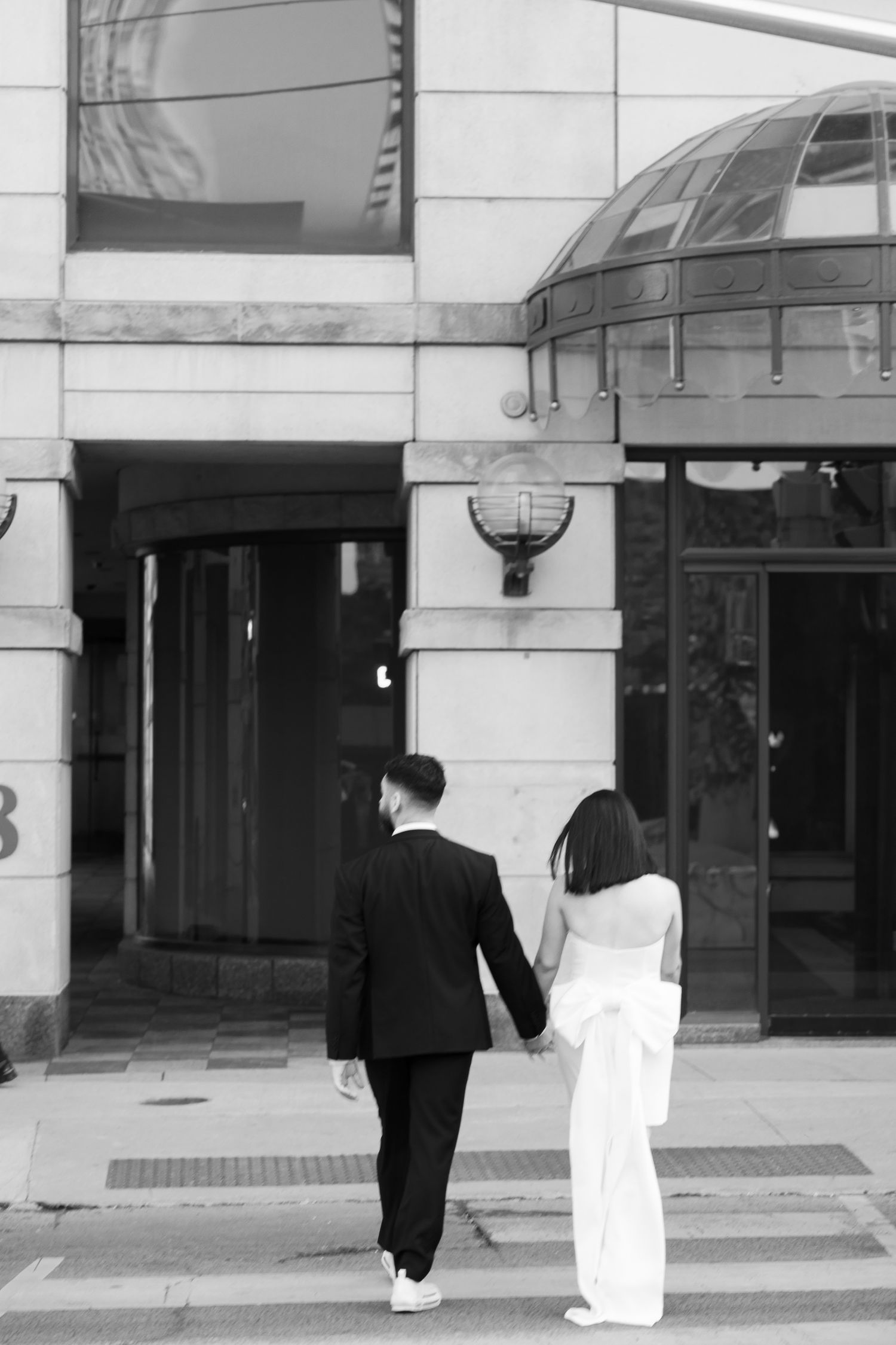 A couple in formal attire walking together outside an urban building entrance.