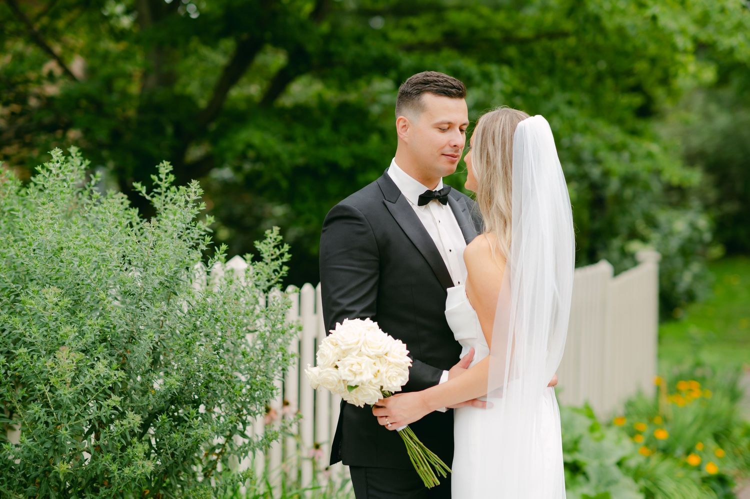 Intimate wedding moment captured in garden setting with white picket fence.