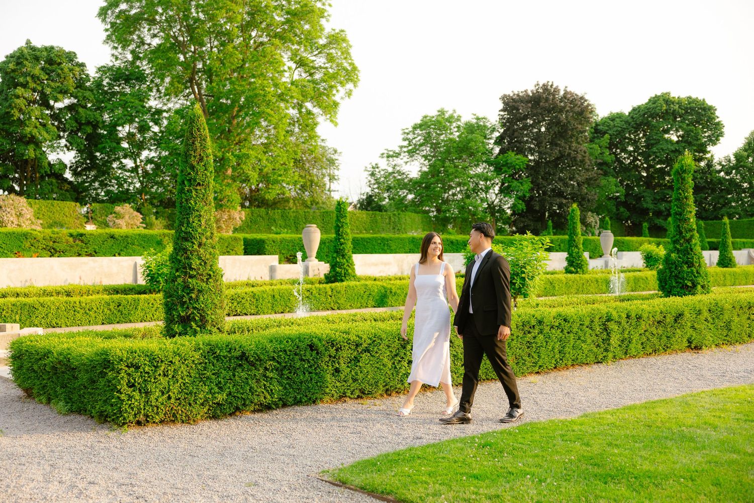 A romantic stroll through a manicured garden with geometric hedges and tall cypress trees.