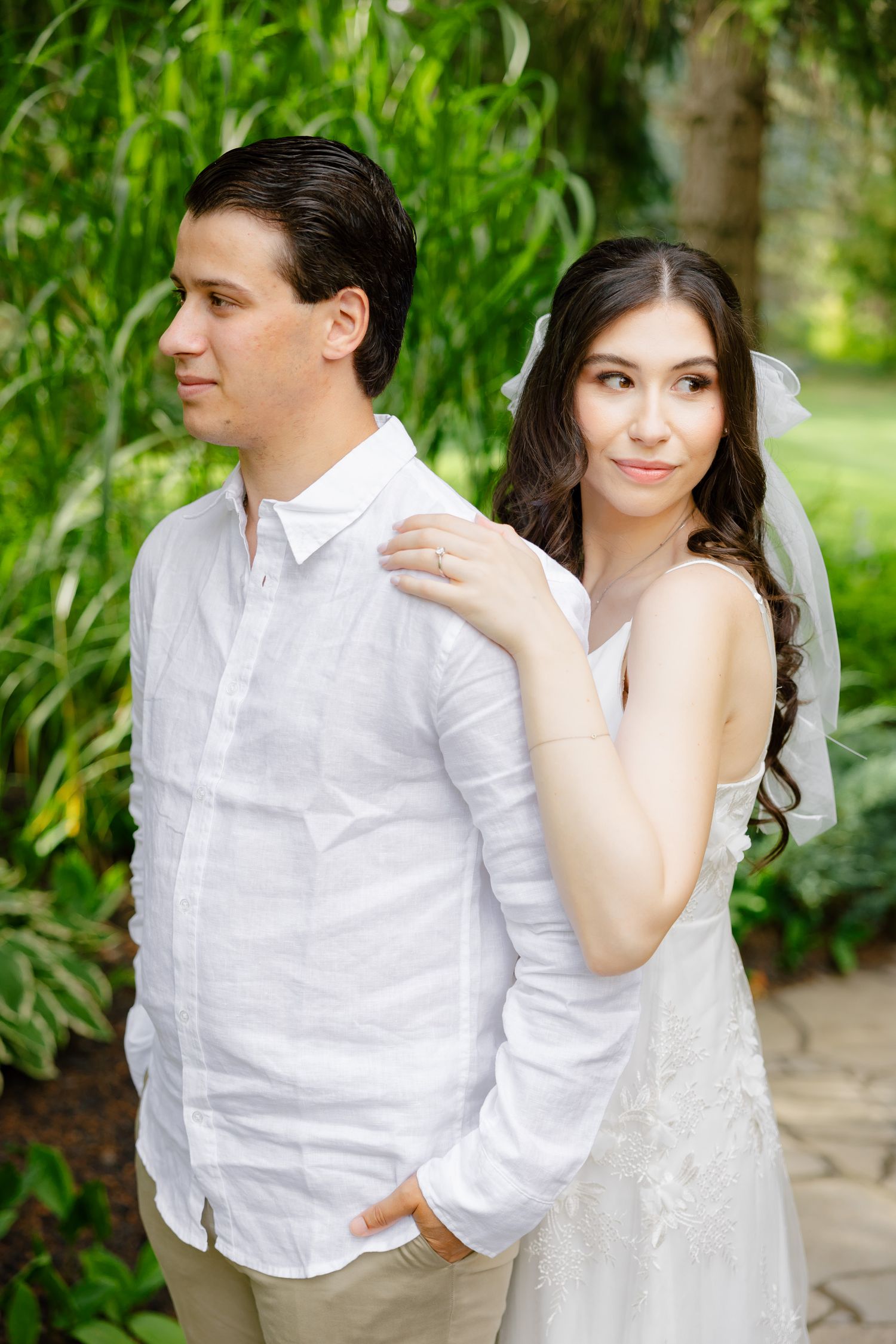 A casual portrait of newlyweds posing in a lush garden setting with natural light.
