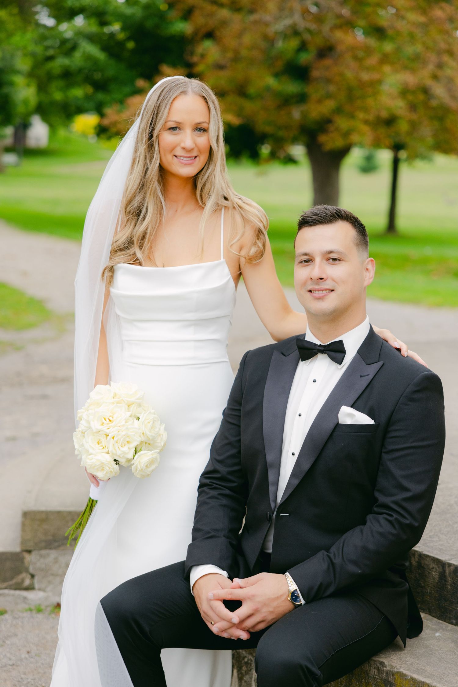 Couple poses for portrait outside historic building with autumn foliage.