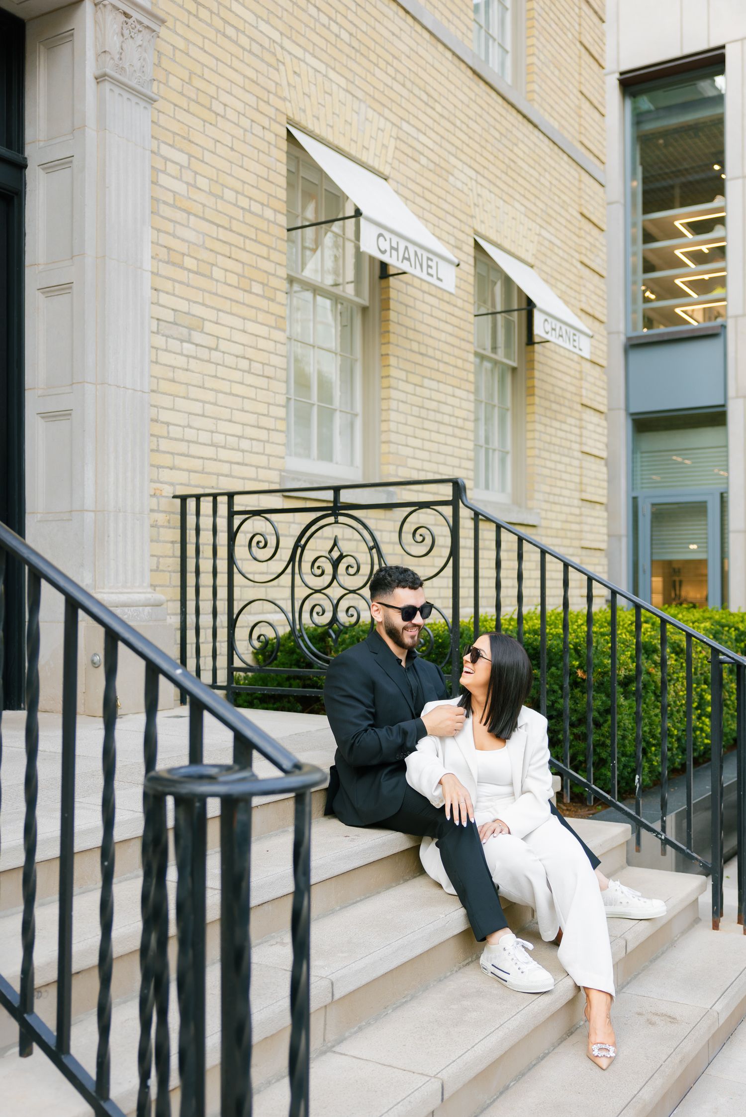 Stylish couple in contrasting outfits share a moment on steps outside a luxury storefront.