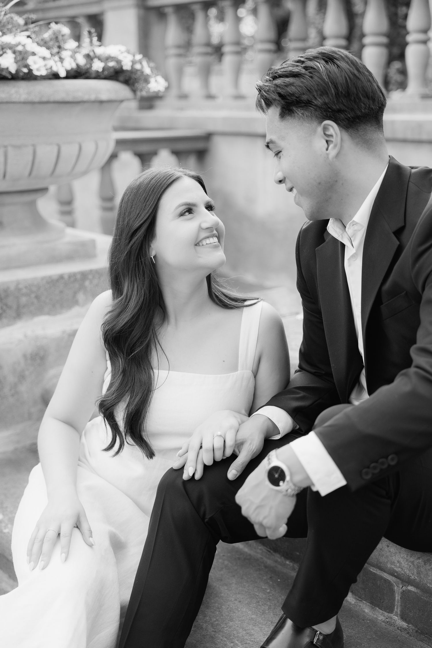 A black and white image of a couple sharing smiles while seated on ornate stone steps.