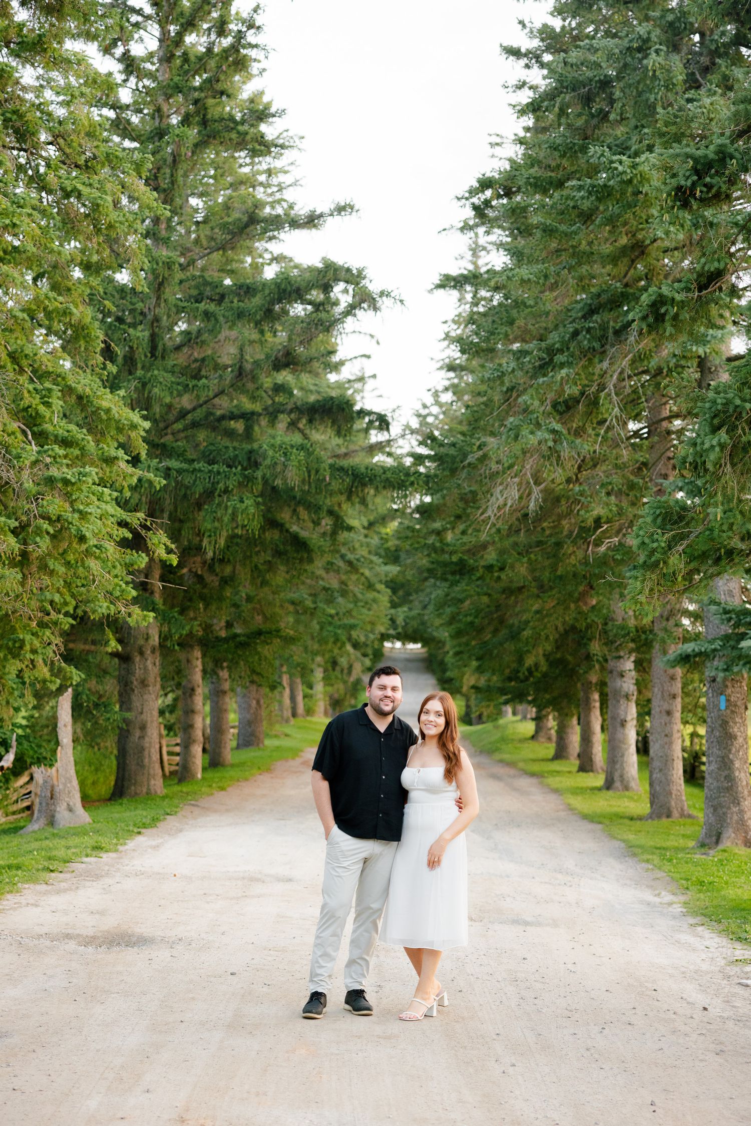 A couple poses for a portrait on a picturesque tree-lined pathway.