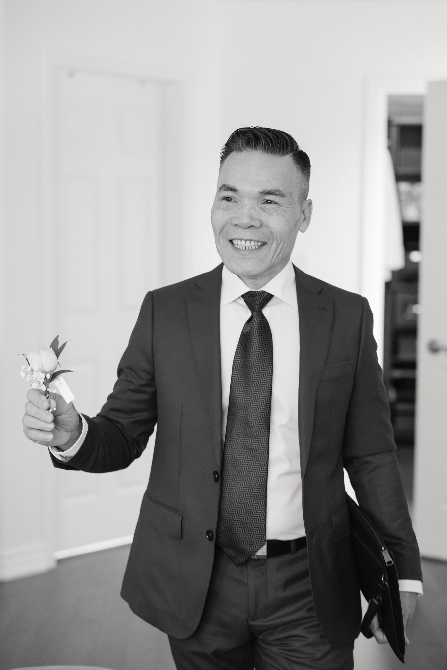 Person in dark suit smiles while holding something in hand during wedding preparations.