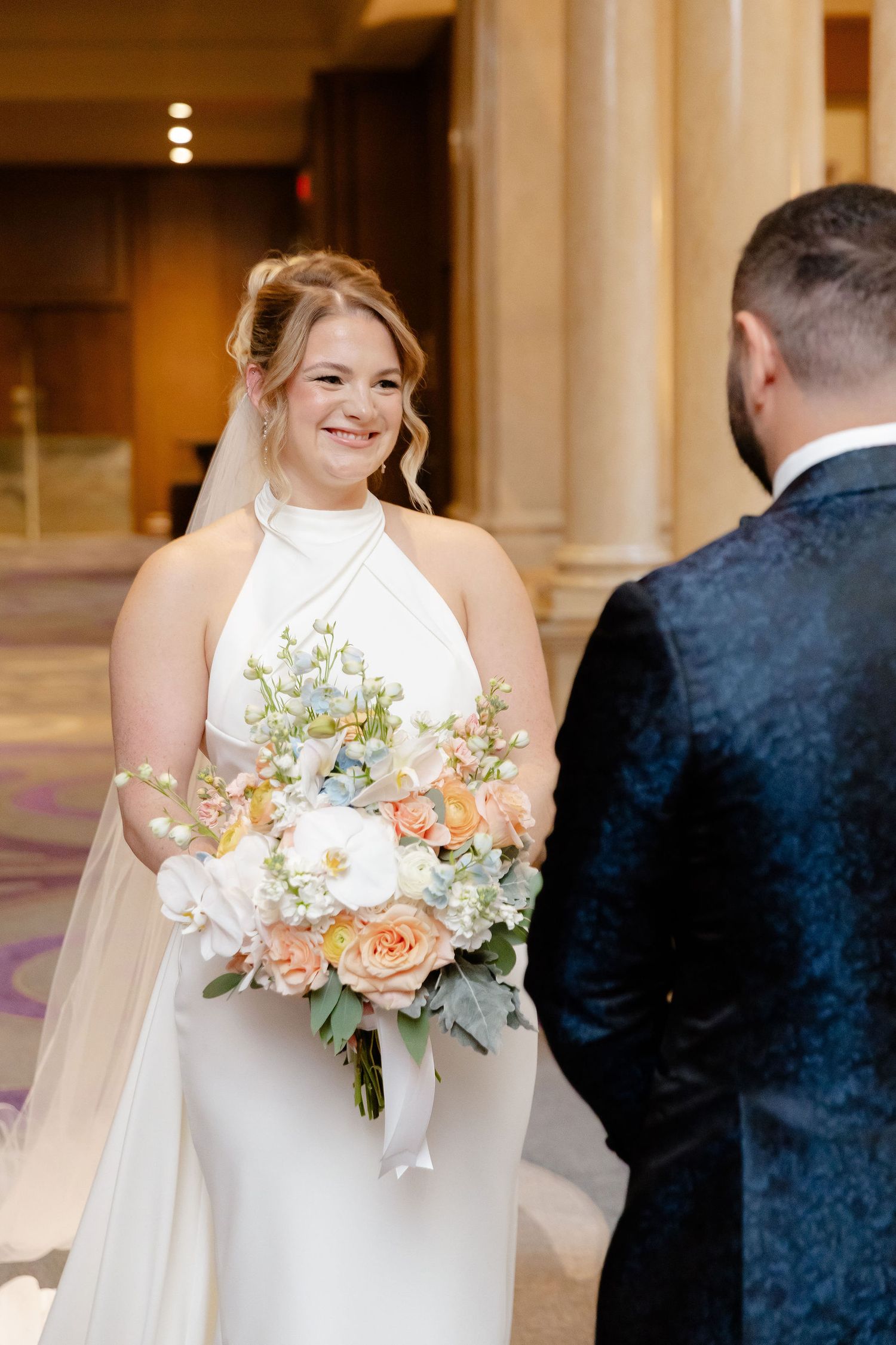 A bride holding a pastel bouquet of roses and eucalyptus during a wedding first look.