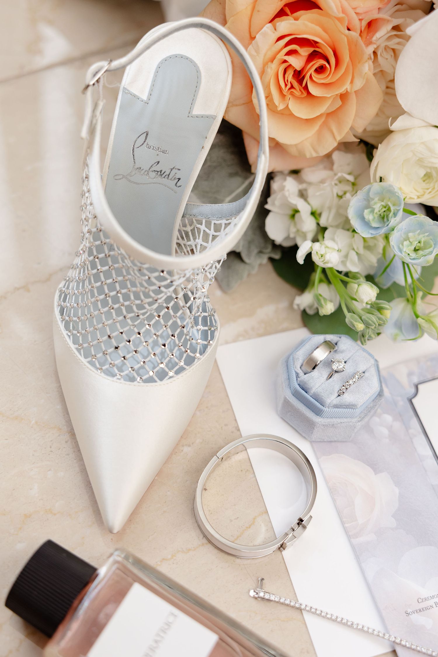 Wedding accessories with peach roses, white shoes, and delicate stationery on a light background.