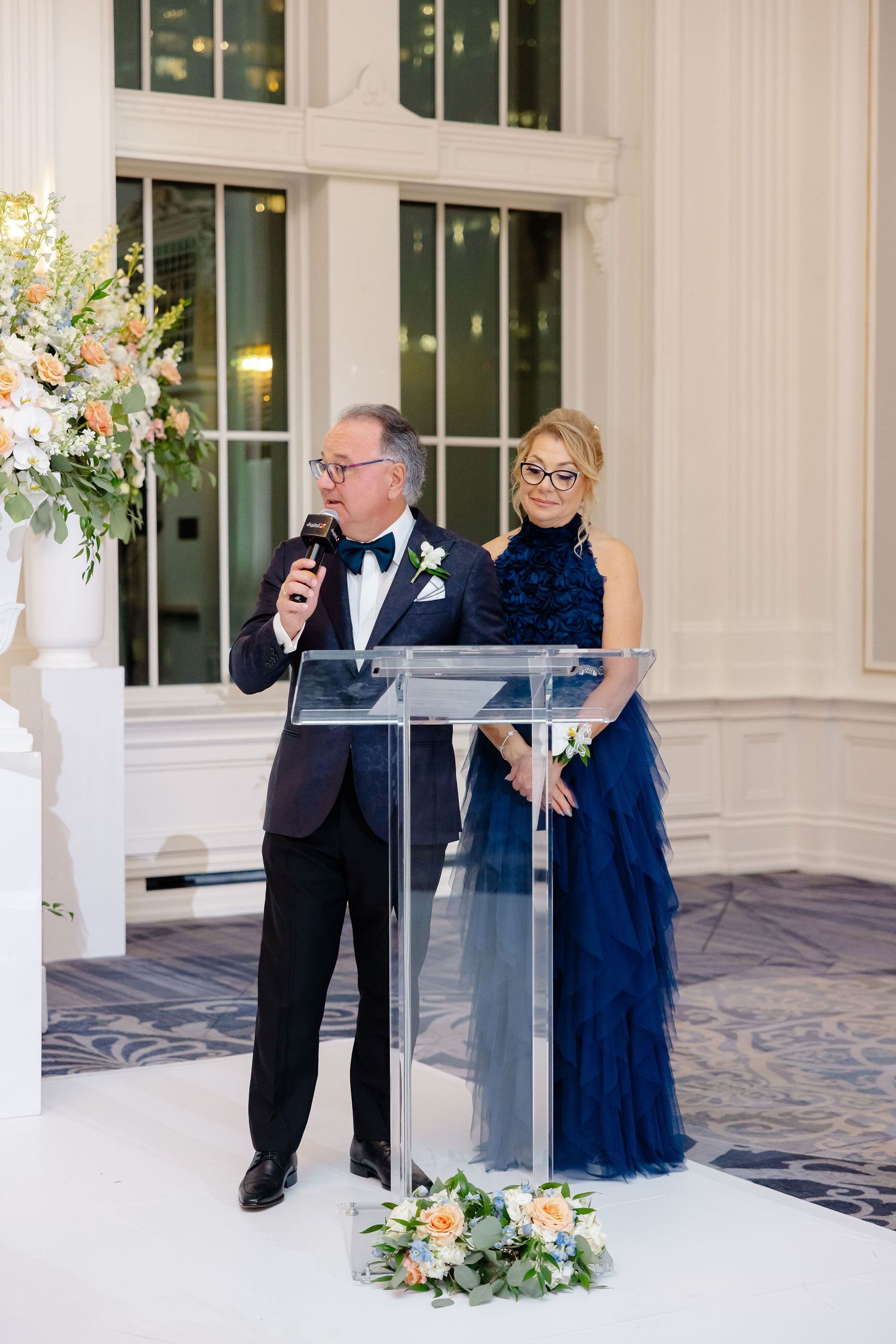 Formal event with speakers at podium in elegant ballroom with floral decor.