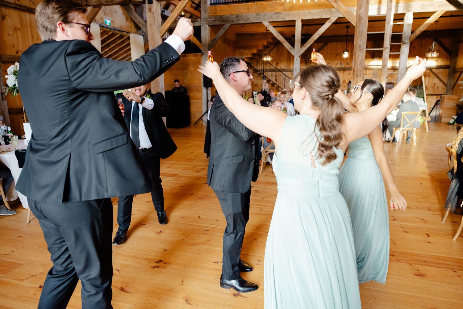 Joyful celebration with dancing guests in formal attire at a barn wedding reception.