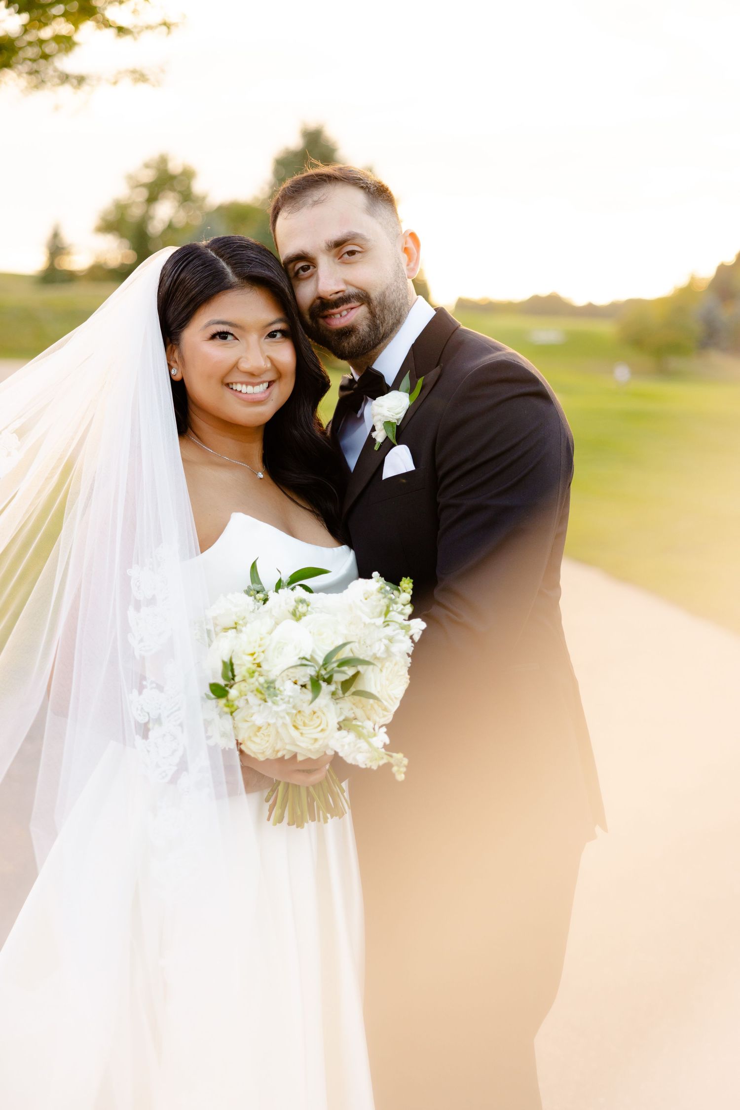 A sunny outdoor wedding portrait of a happy couple with white floral bouquet on a golf course.