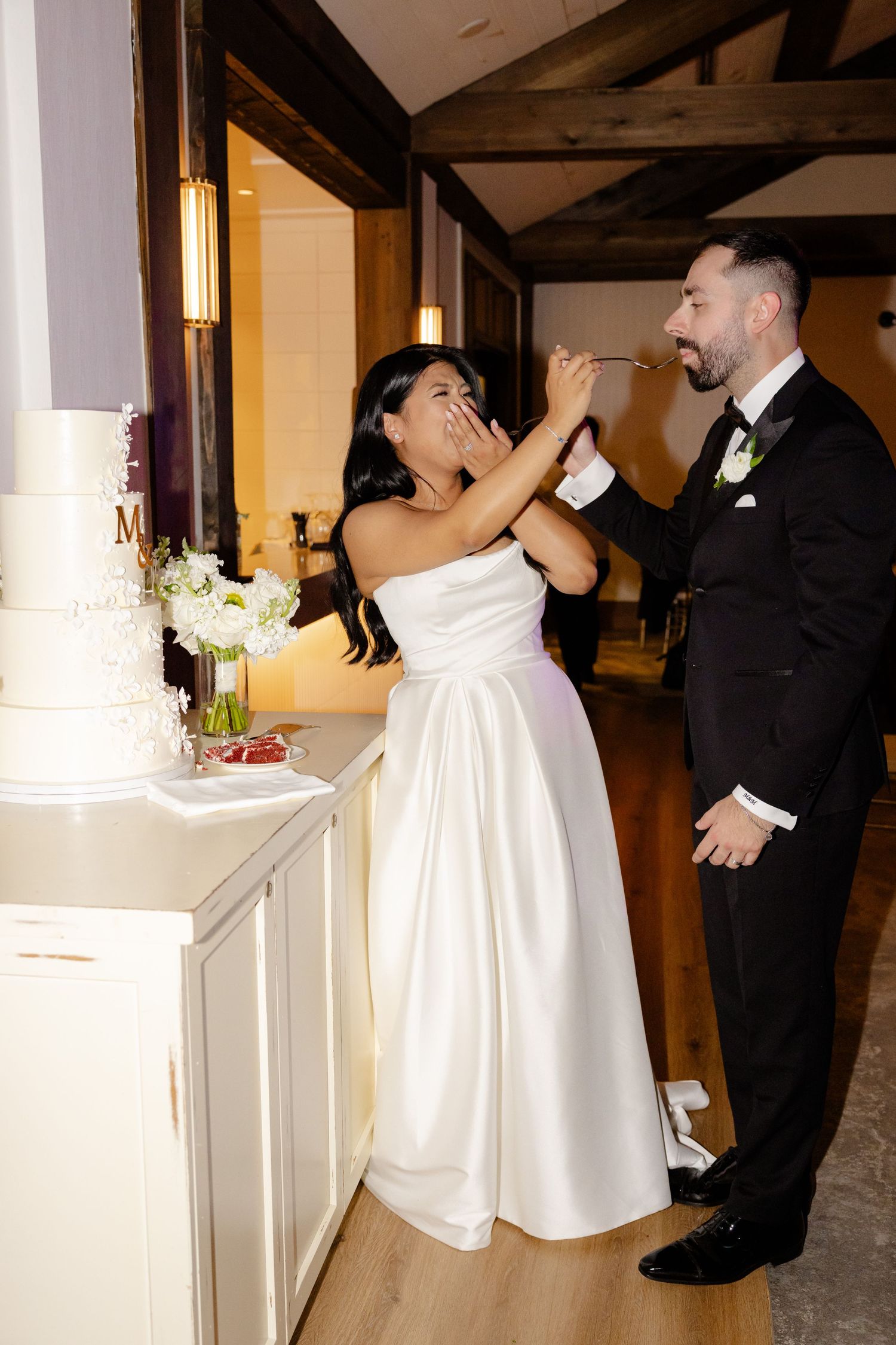 Playful moment as newlyweds feed each other wedding cake at reception.