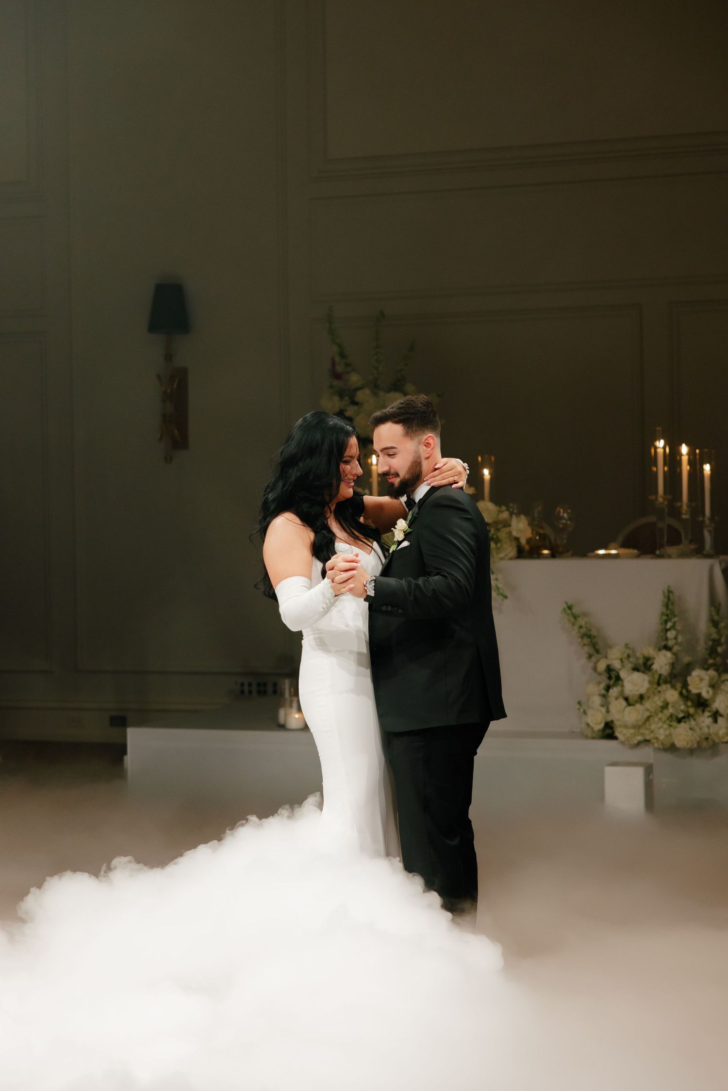 Intimate dance moment in elegant venue with candlelit backdrop and low-lying fog effects.