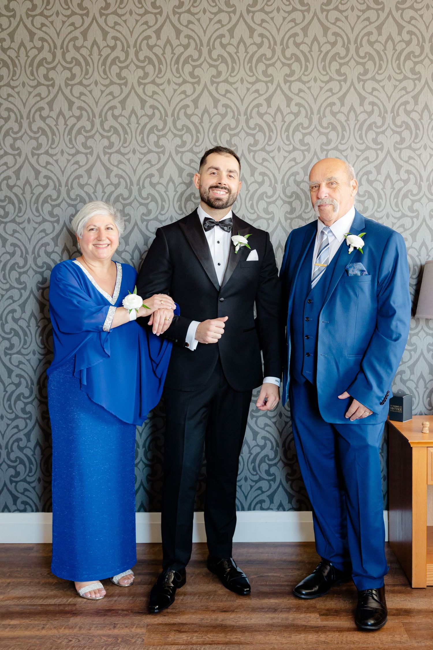 Family portrait with people in formal attire standing against a grey damask wallpaper.