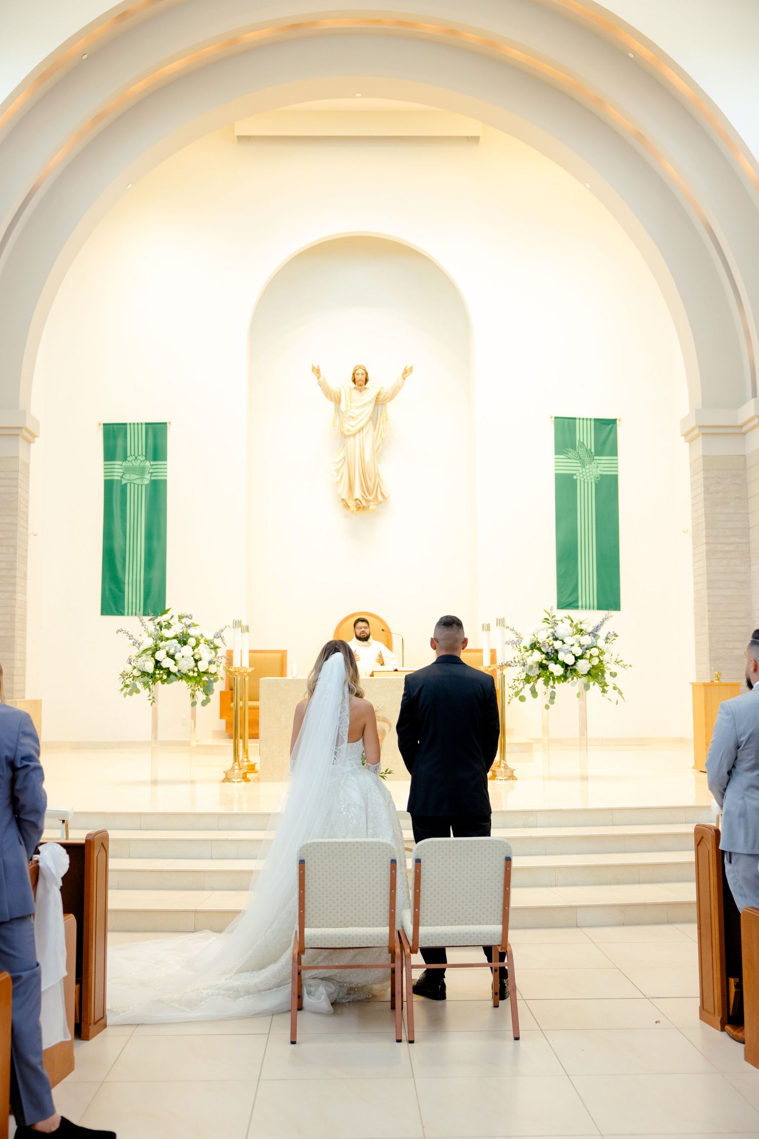 A wedding ceremony in a church with green shutters and a white Jesus statue at the altar.