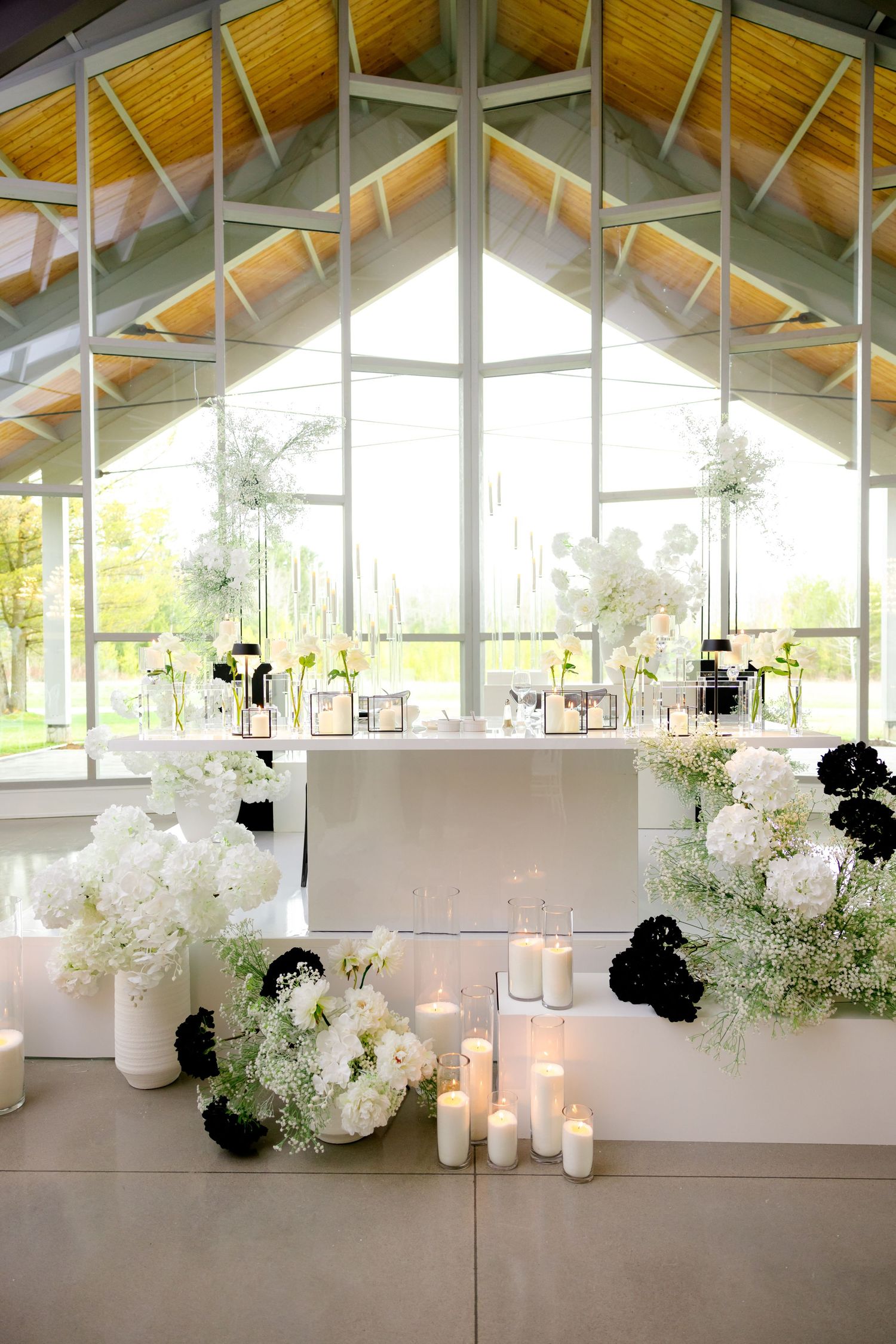 Modern chapel venue with white floral arrangements and candles against large windows.