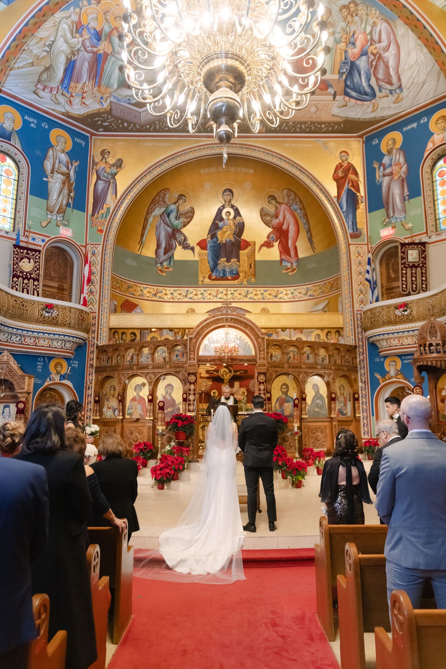 Orthodox church wedding ceremony in an ornate sanctuary with blue walls, religious frescoes, and a grand chandelier.