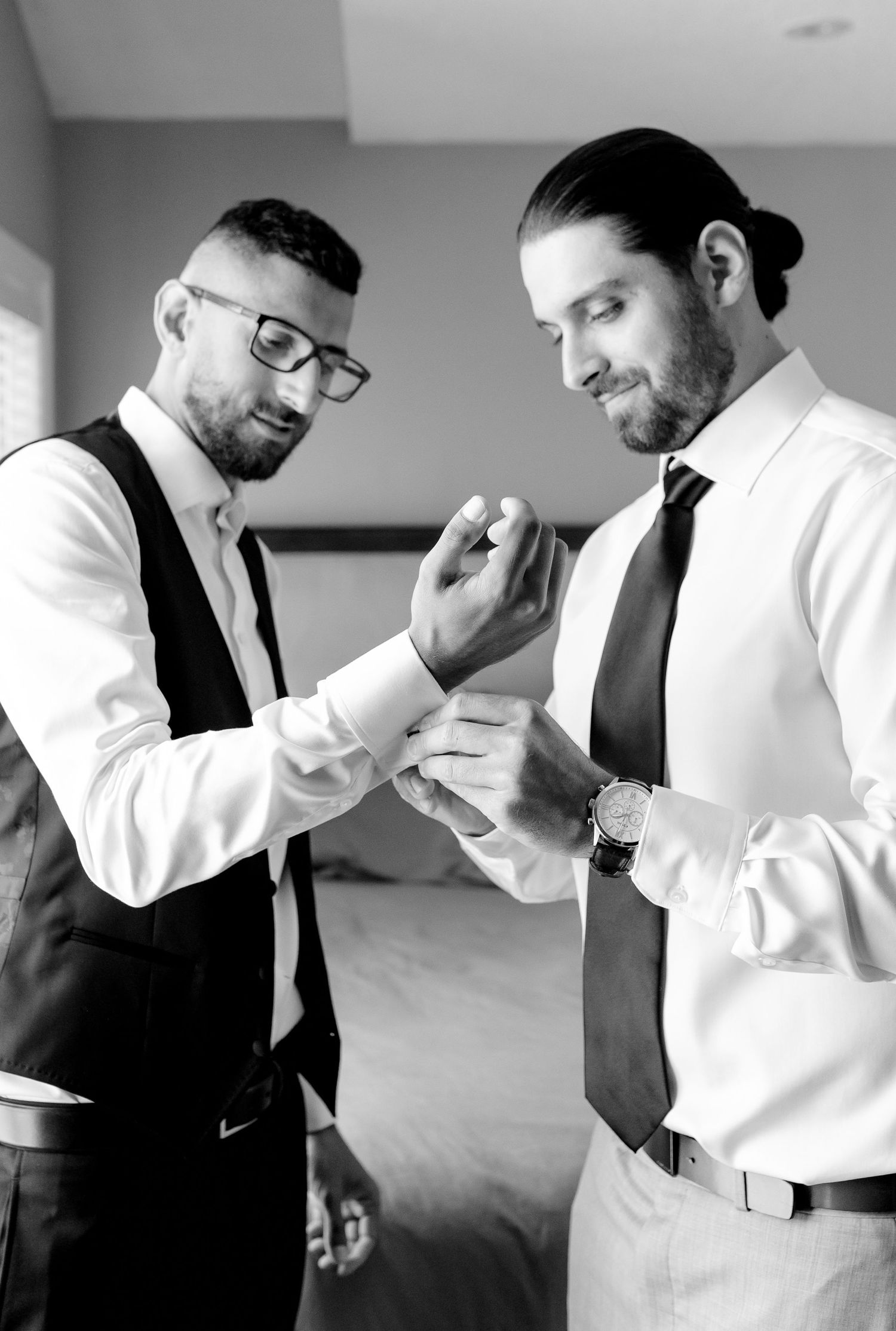 Two people in formal attire assist each other with wedding preparations.