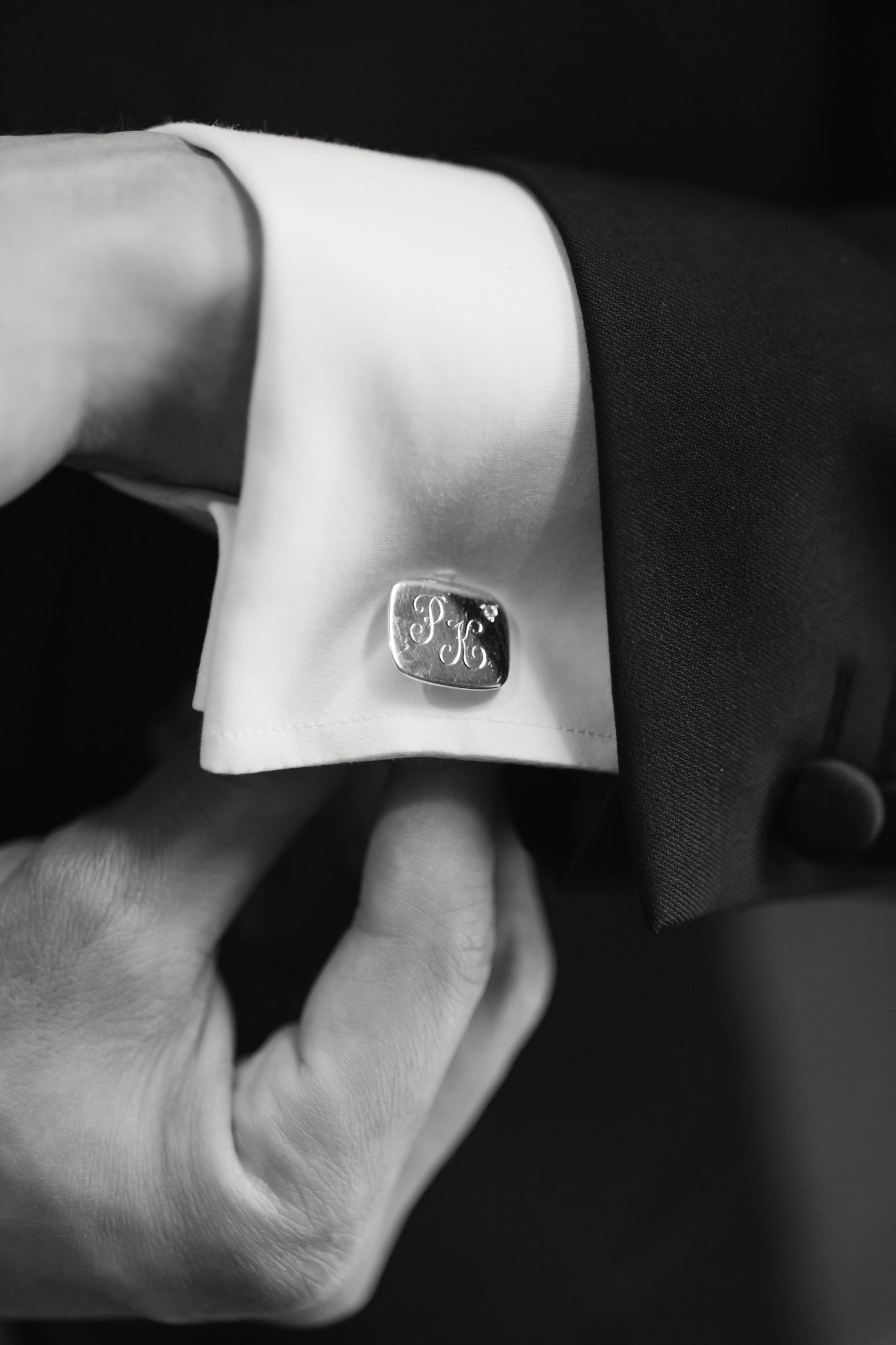 Close-up black and white photo of a monogrammed cufflink on a white dress shirt sleeve.