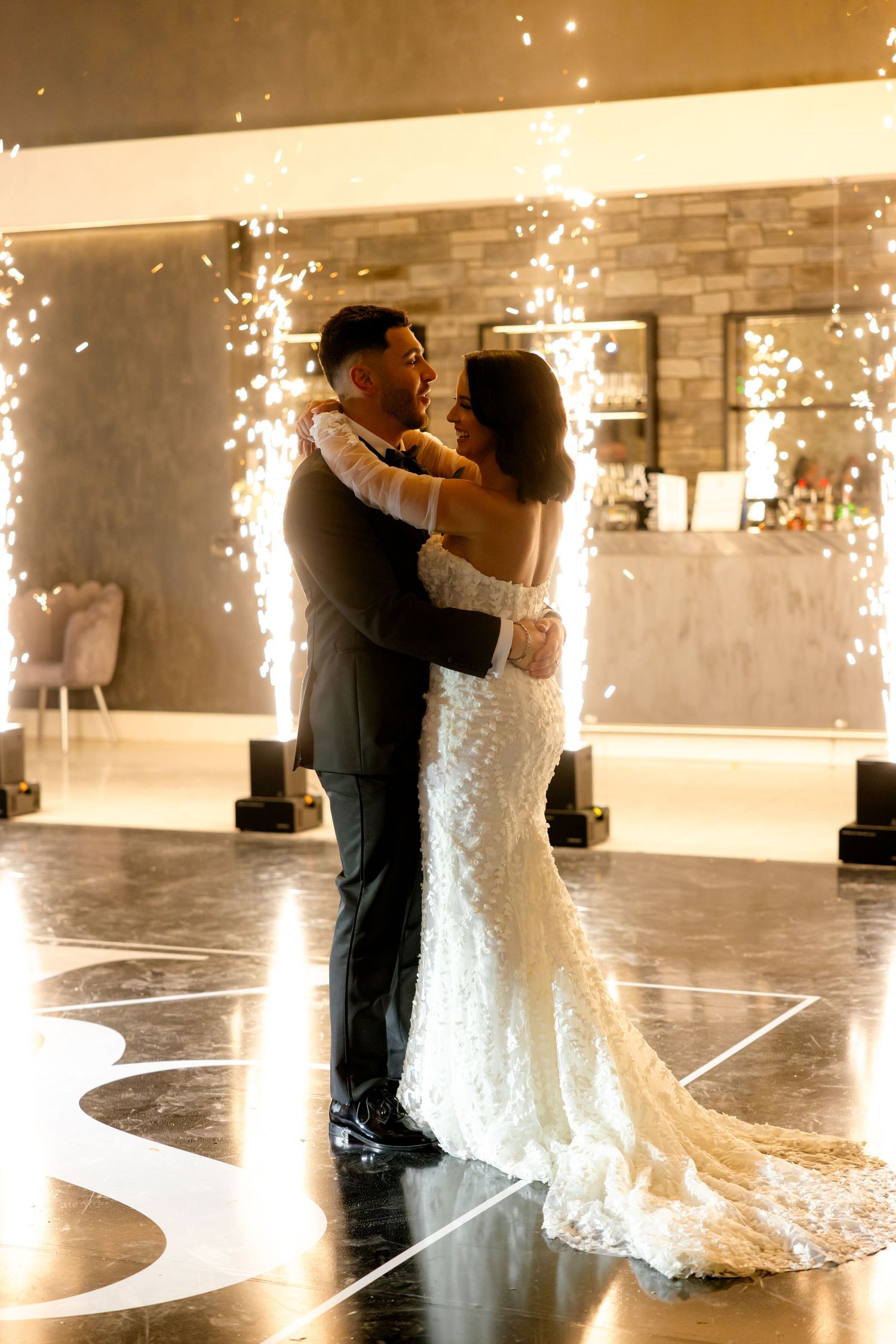 A romantic first dance moment with sparklers illuminating the background at a modern wedding venue.