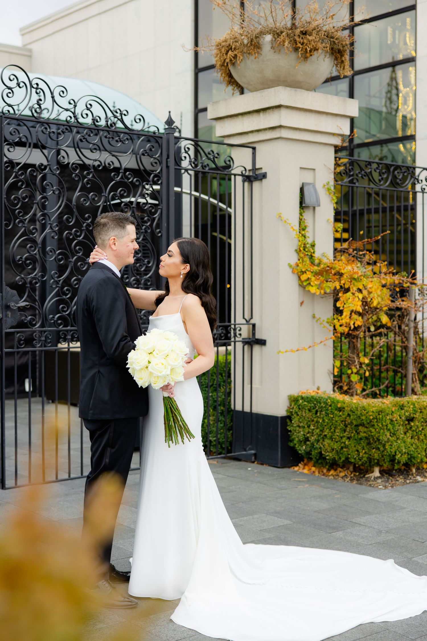 Couple shares intimate moment in front of ornate gates with yellow autumn leaves.