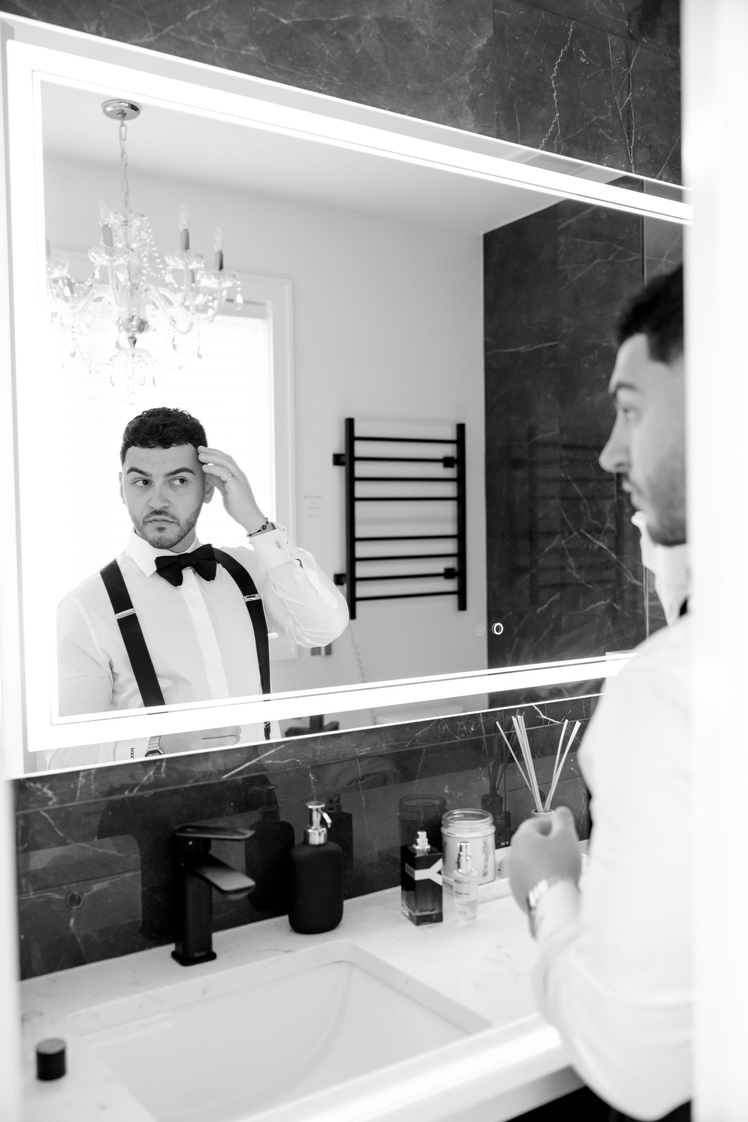 Mirror reflection of formal attire with bow tie and suspenders in modern bathroom.