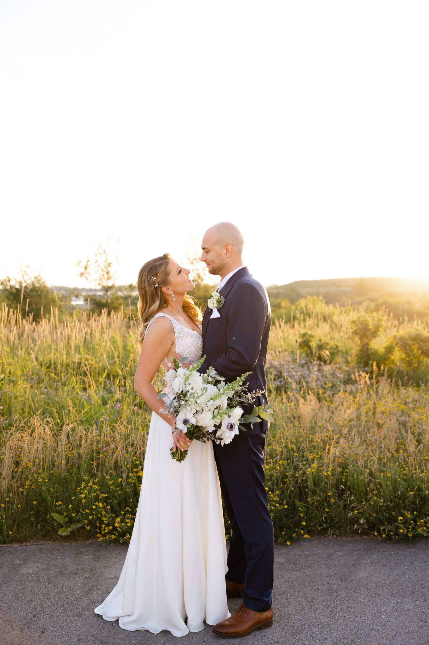 A couple shares an intimate moment at sunset holding a white floral bouquet on their wedding day.