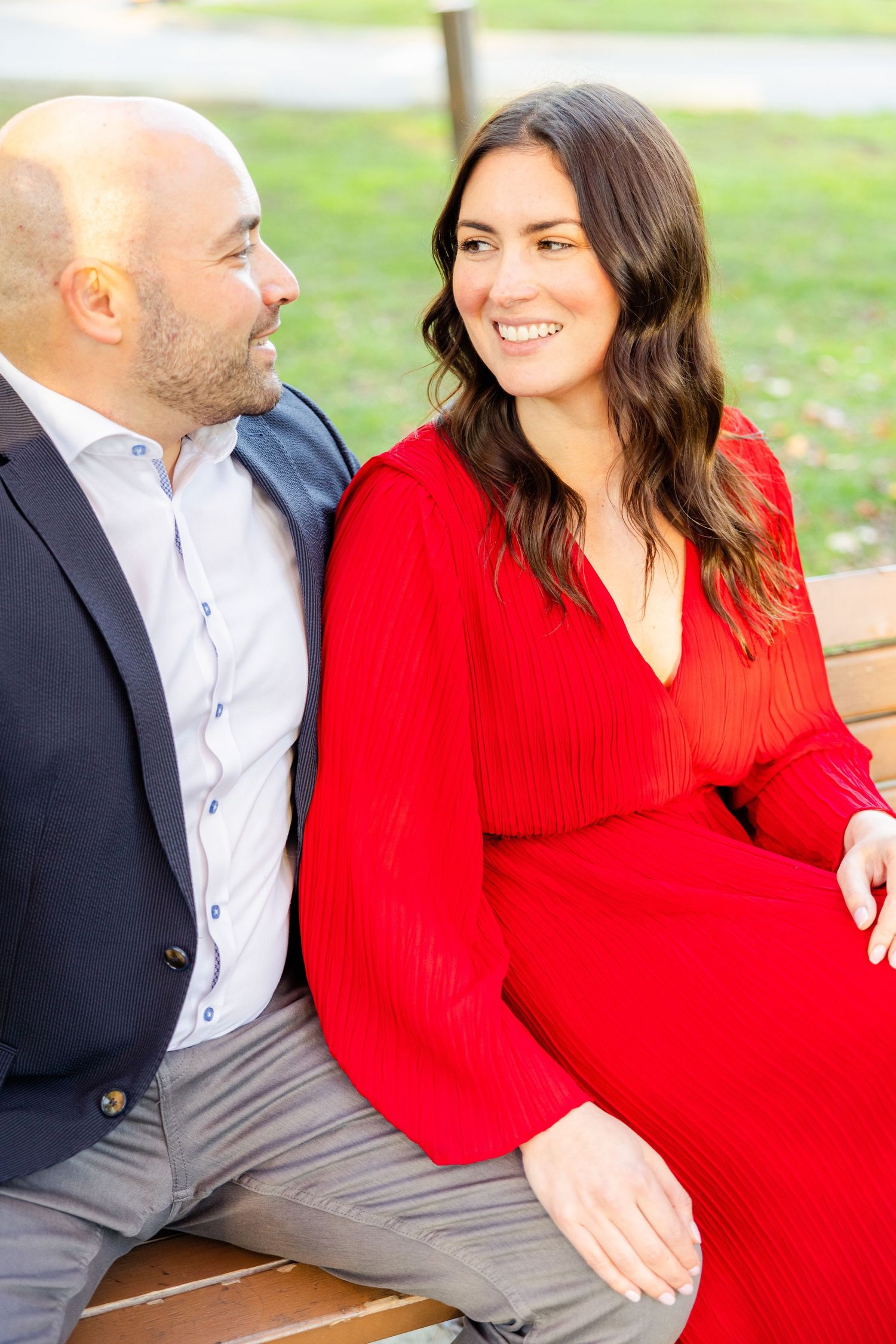 Romantic portrait of couple on park bench, she in red dress and he in dark blazer.