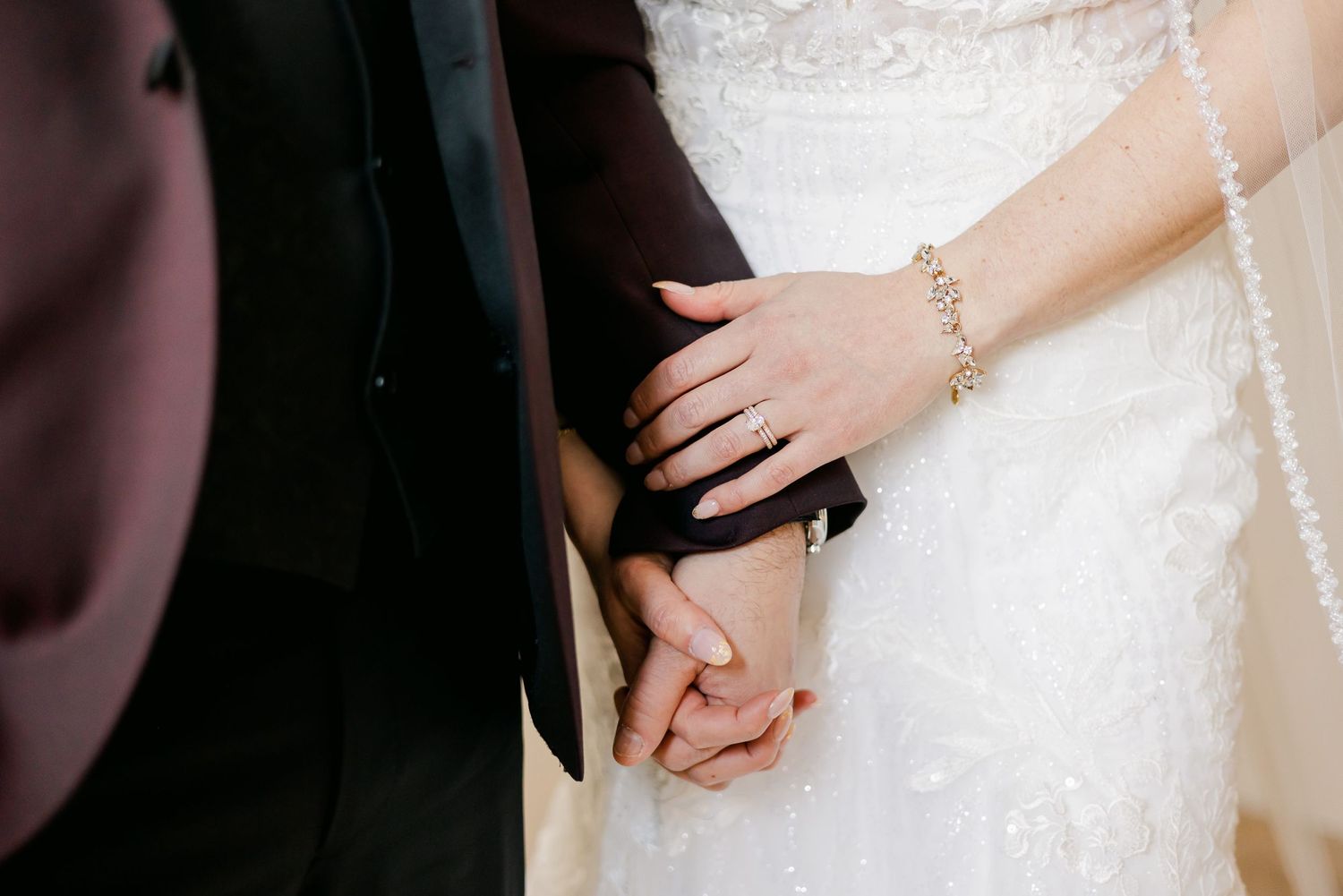 Close-up of couple holding hands showing wedding day jewelry and attire.