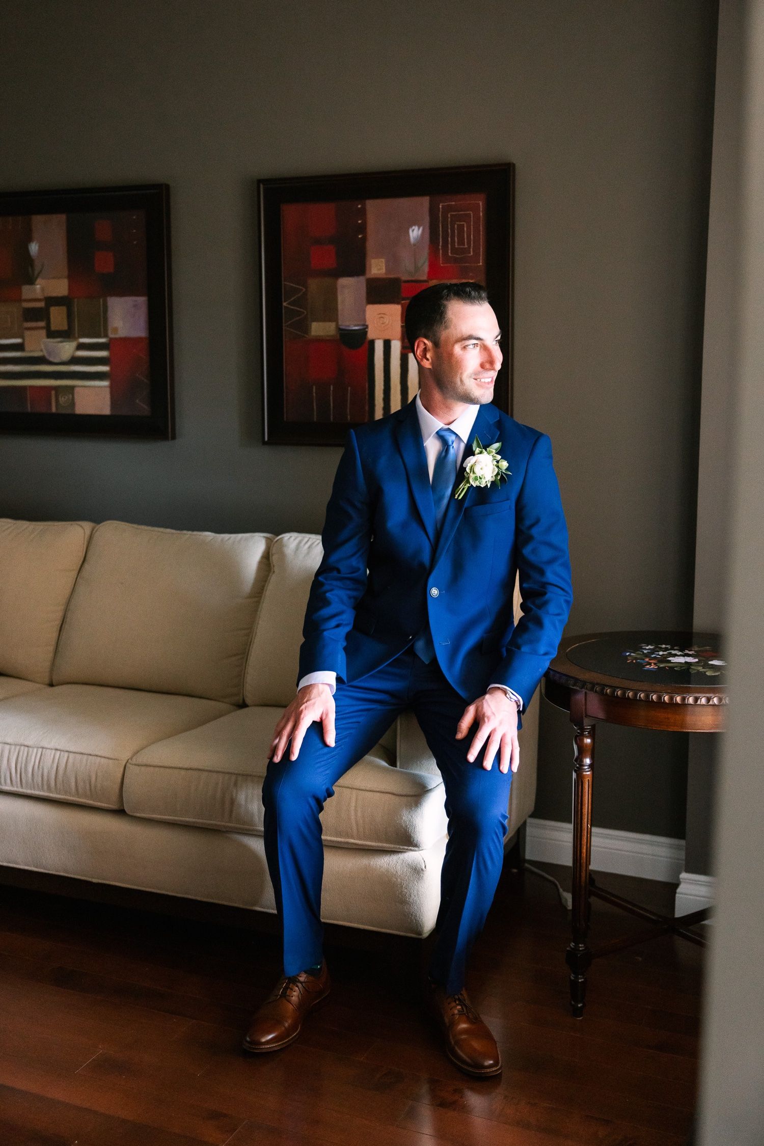A person in a crisp blue suit sits elegantly on a beige couch with abstract art in background.