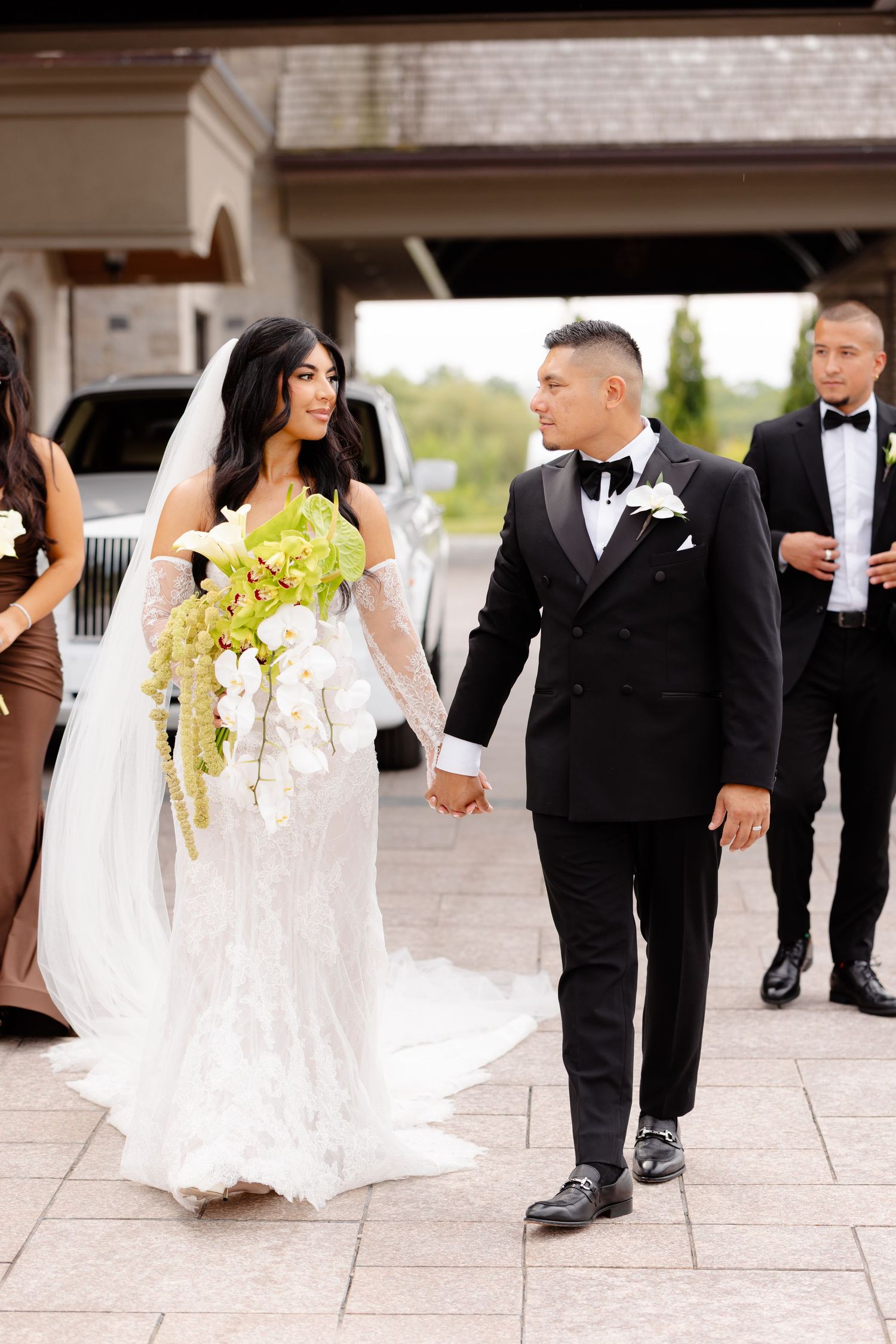 Wedding party members walk together on stone patio showing formal attire and flowing dresses.