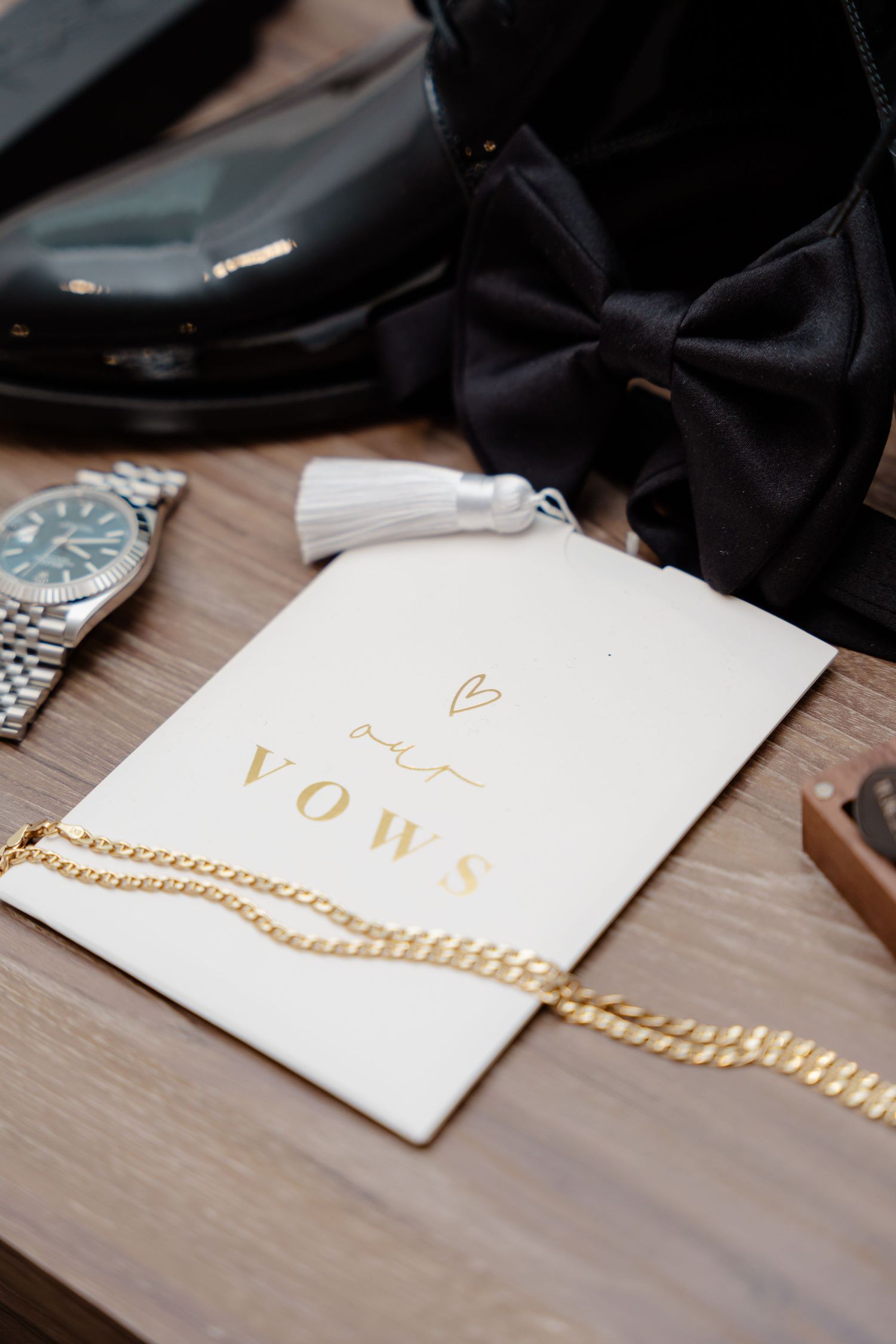 Wedding vows card with gold chain and luxury watch on wooden surface.