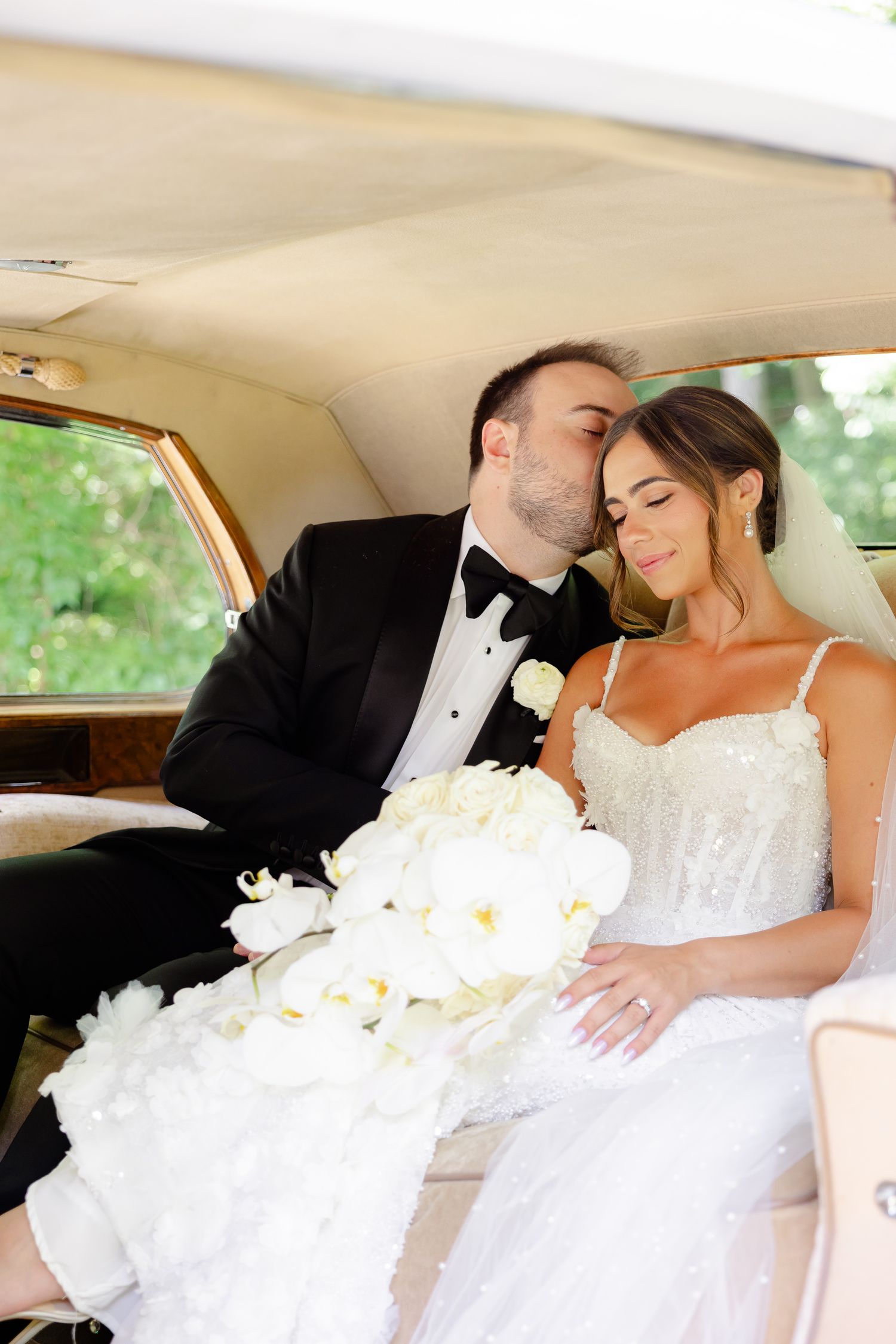 A romantic moment between a couple in wedding attire sitting in the backseat of a classic car.