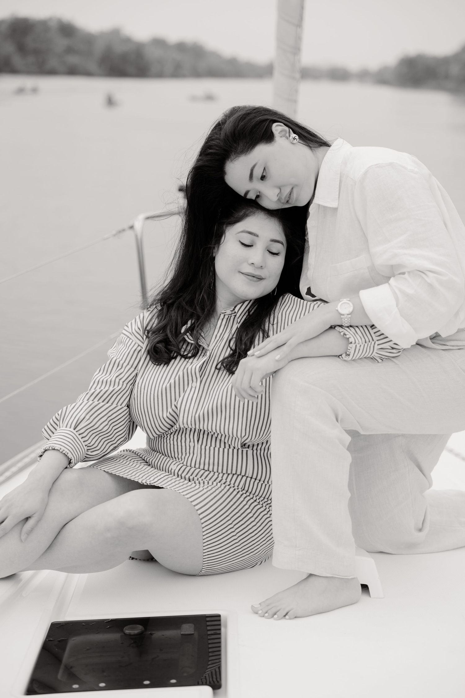 A couple in white and striped outfits share a tender moment on a boat deck in black and white photography.