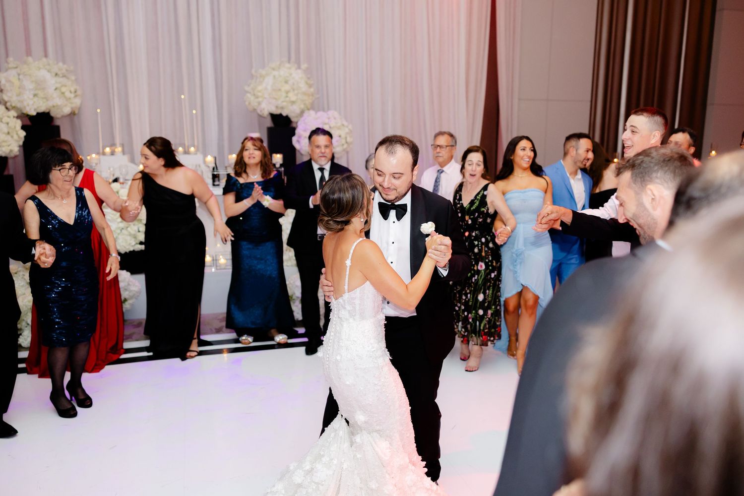 A couple shares their first dance at a wedding reception while guests watch and celebrate from the sidelines.