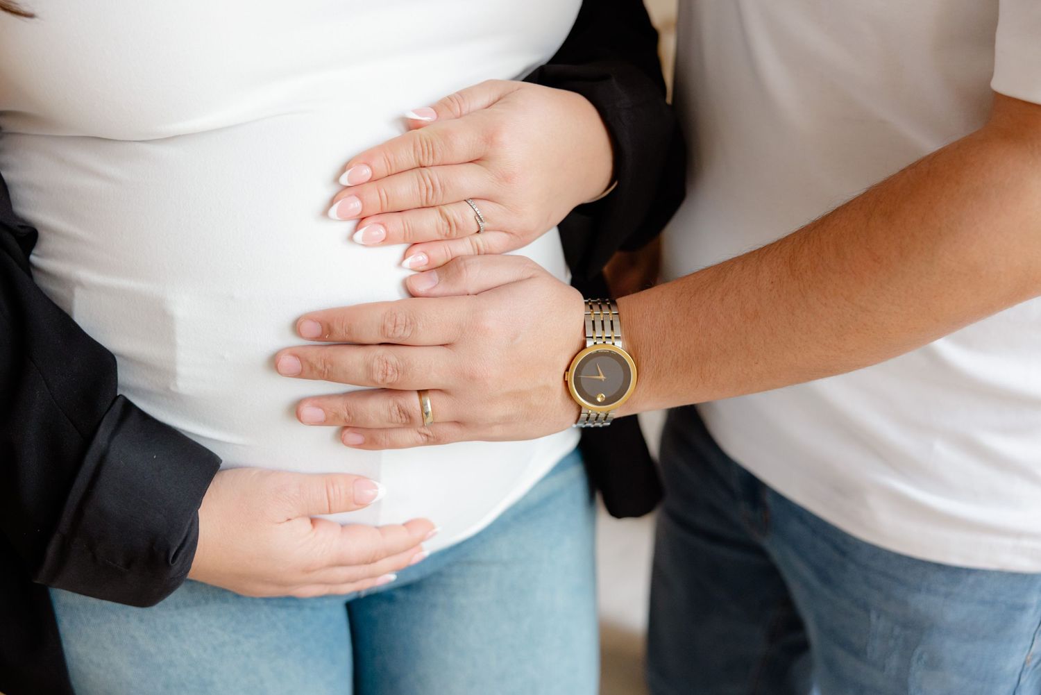 Close-up of hands cradling a pregnant belly while wearing a gold wristwatch.