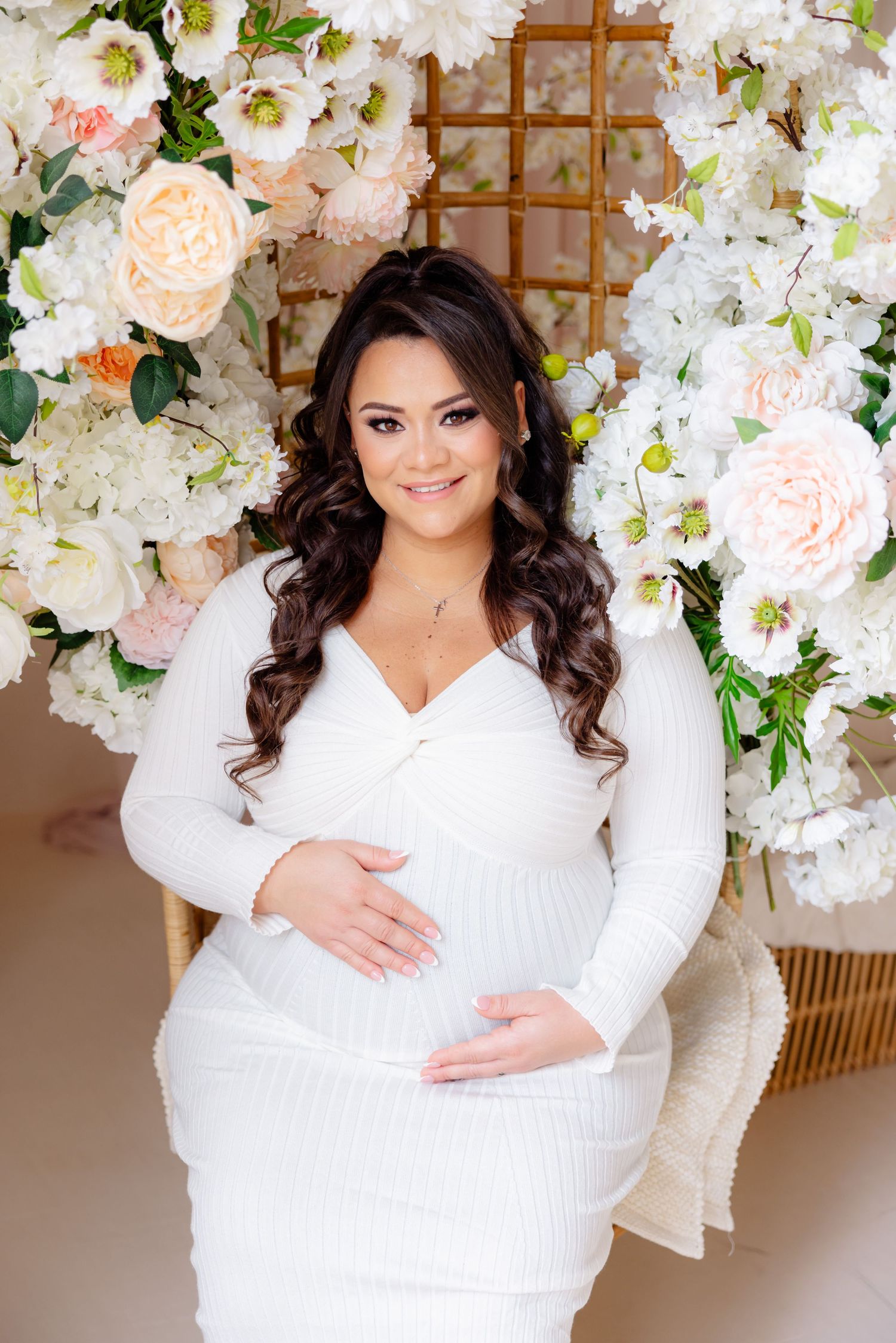 Beautiful maternity photo with white dress against floral backdrop of roses and orchids in soft pink and white tones.