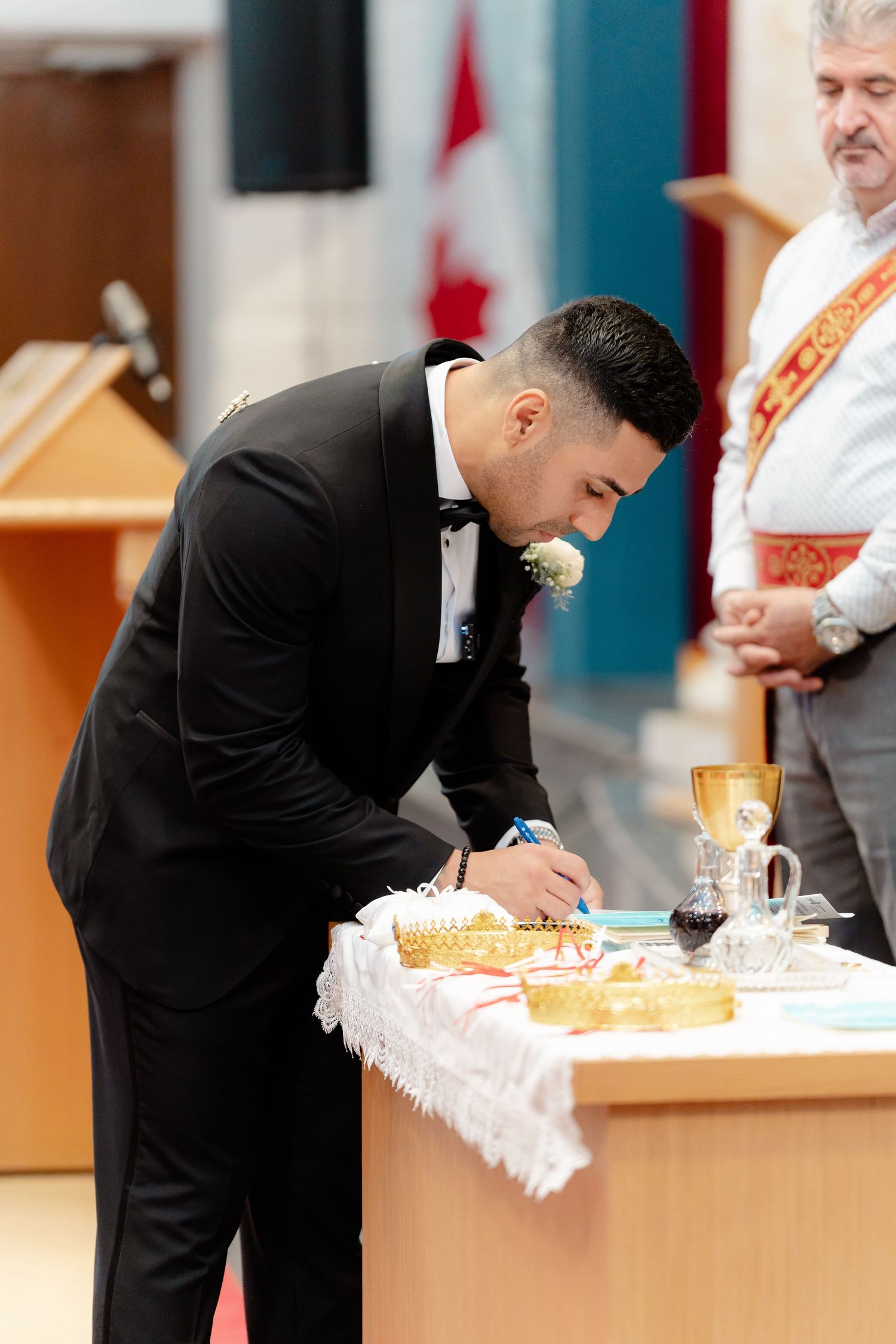 Groom in black tuxedo signs documents at altar during wedding ceremony.