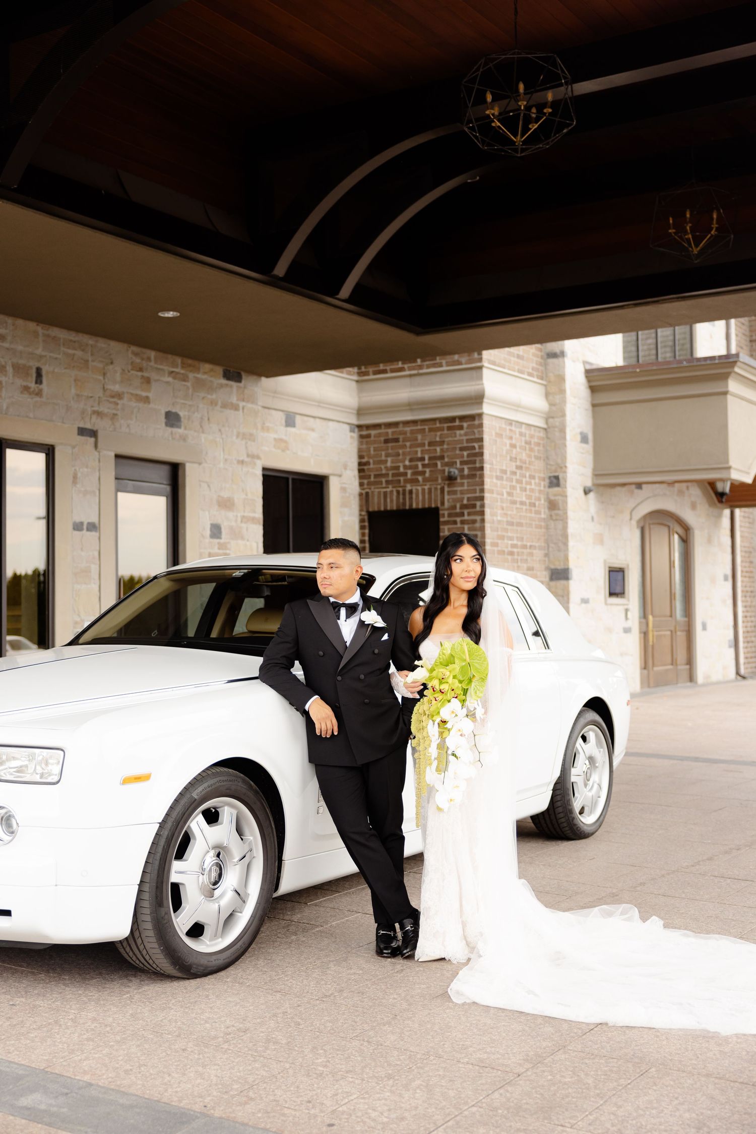 White sports car parked under a covered driveway with a couple in wedding attire posing dramatically next to it.