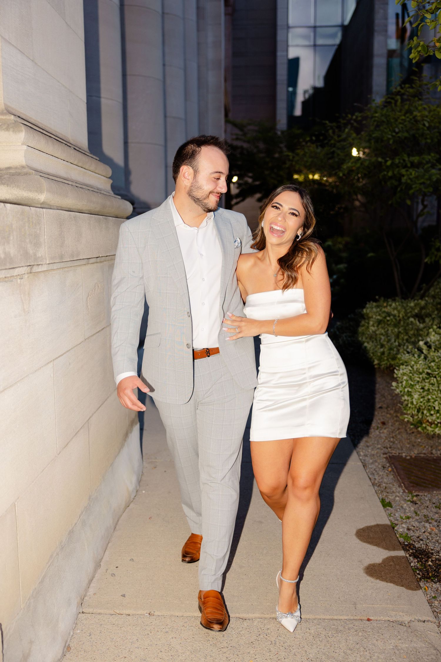 Joyful couple sharing laughs while walking along building exterior.