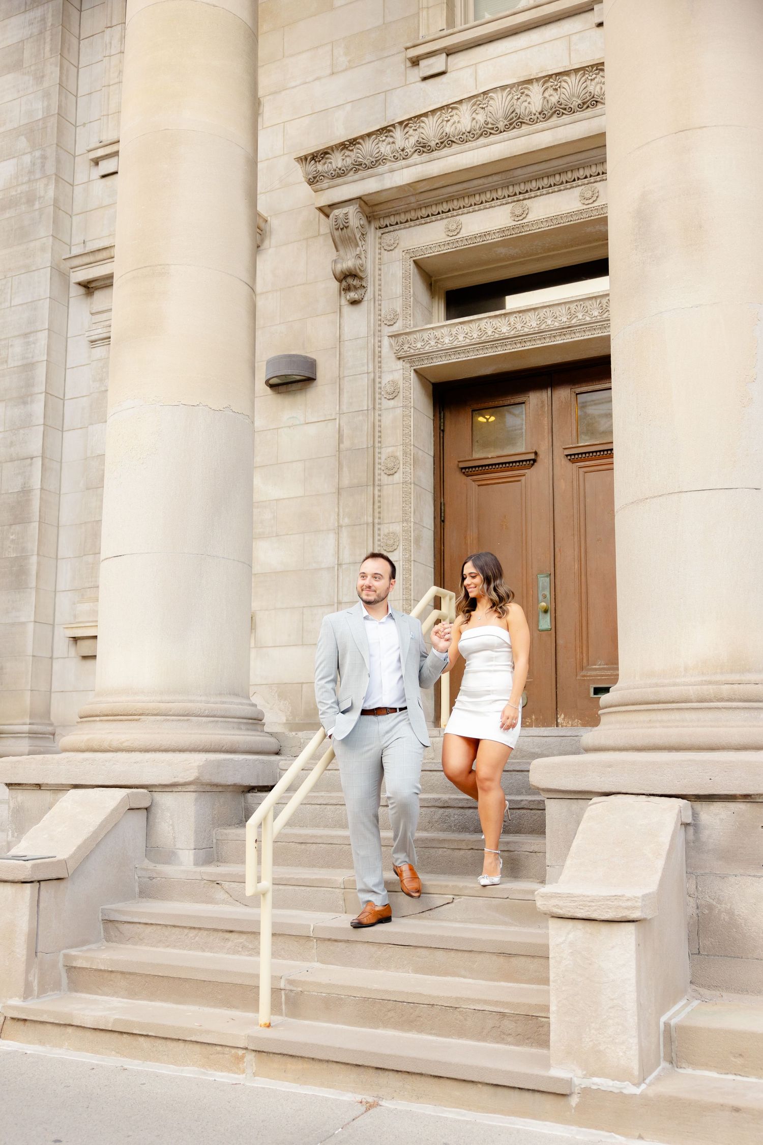 A couple descends stone steps of a classic building entrance with large columns.