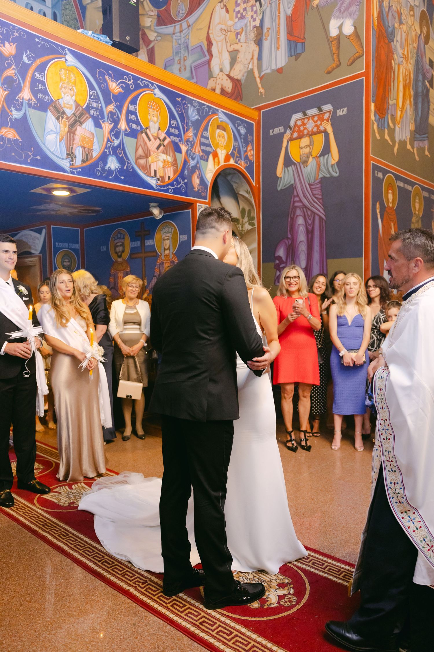 Wedding ceremony in progress within beautifully decorated Orthodox church with painted murals.