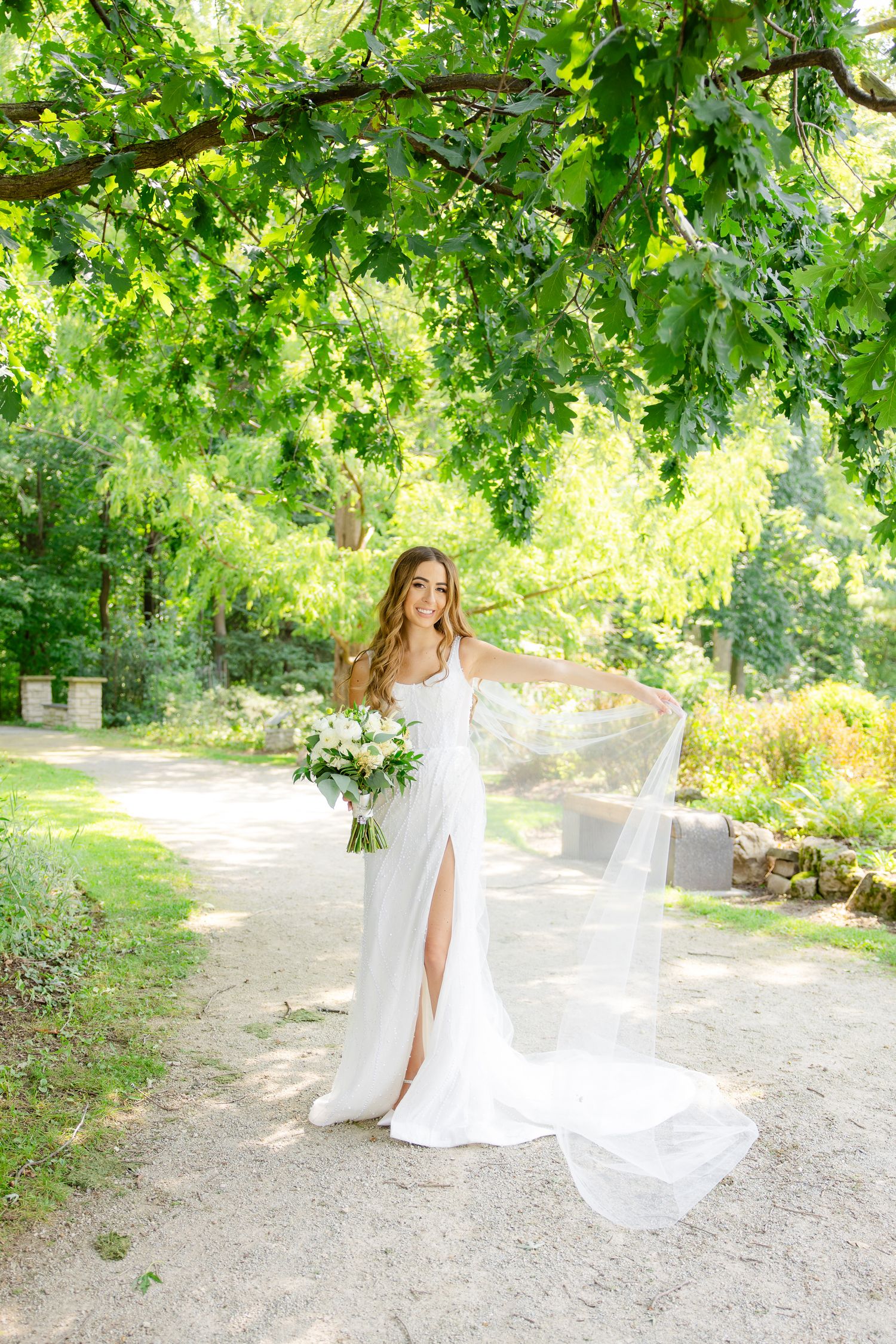 An elegant bridal portrait under green tree canopy on a garden path.