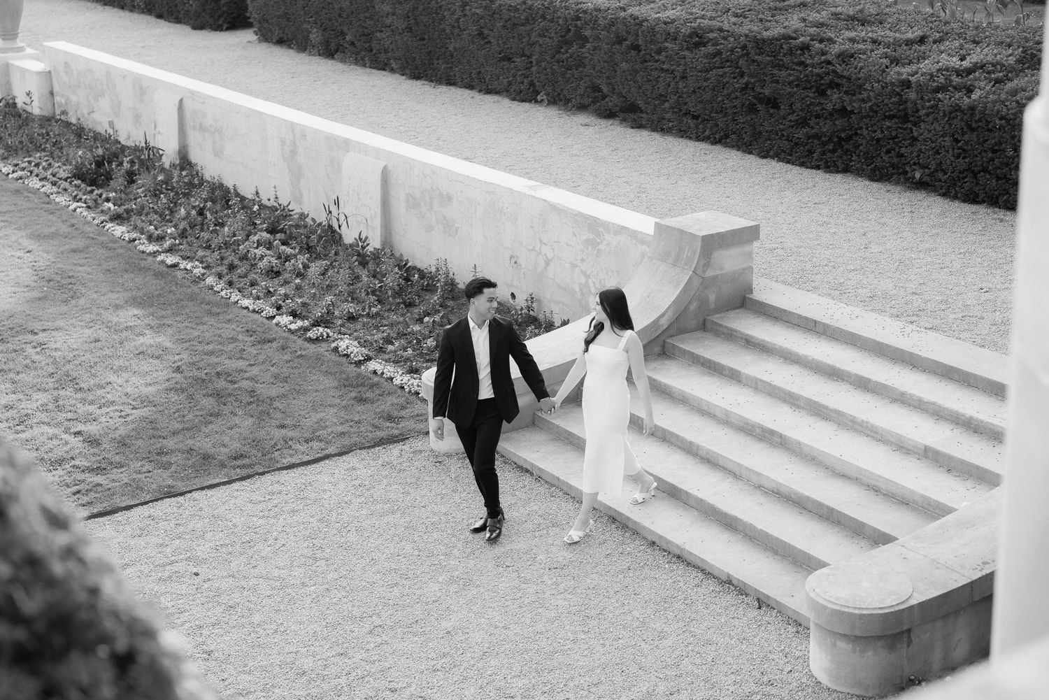 A black and white photo captures two individuals ascending stone steps in a formal garden setting.