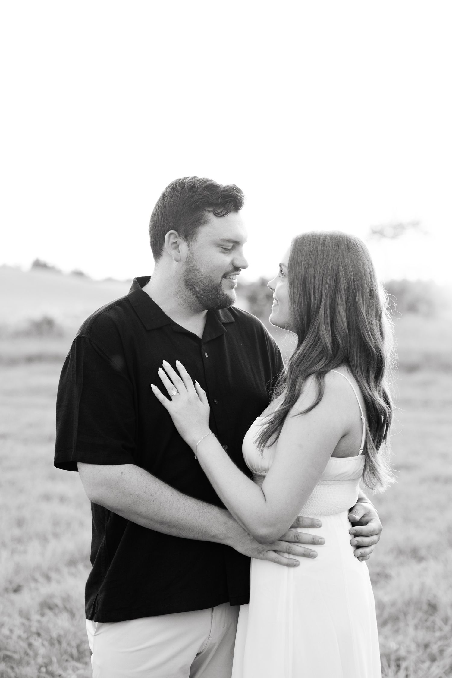 A black and white intimate portrait of a couple embracing in an outdoor setting.